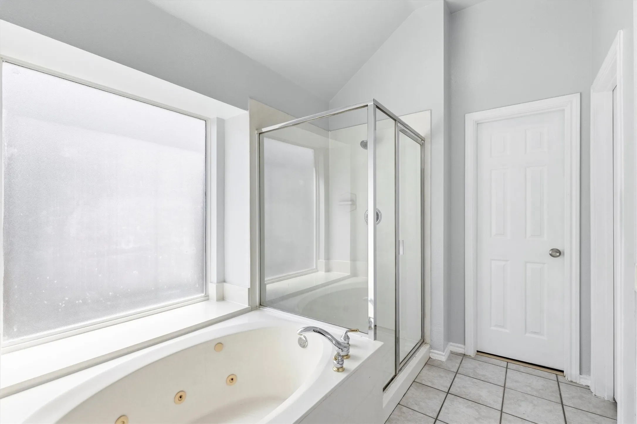 Bathroom featuring a jetted soaking tub, glass-enclosed shower, white paneled door, and tiled flooring