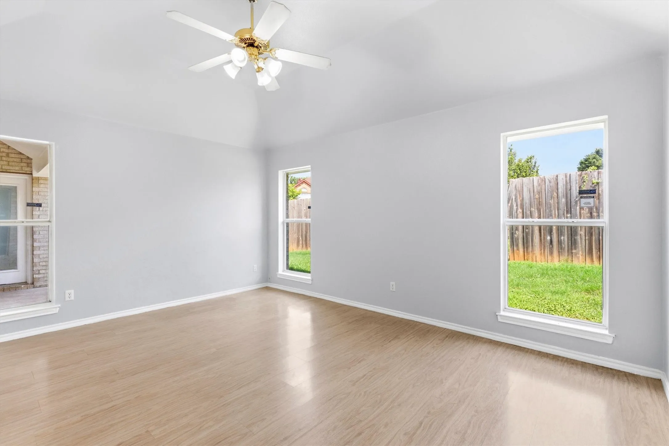 Spacious room featuring wood-finish flooring, vaulted ceilings, and a ceiling fan with integrated lighting