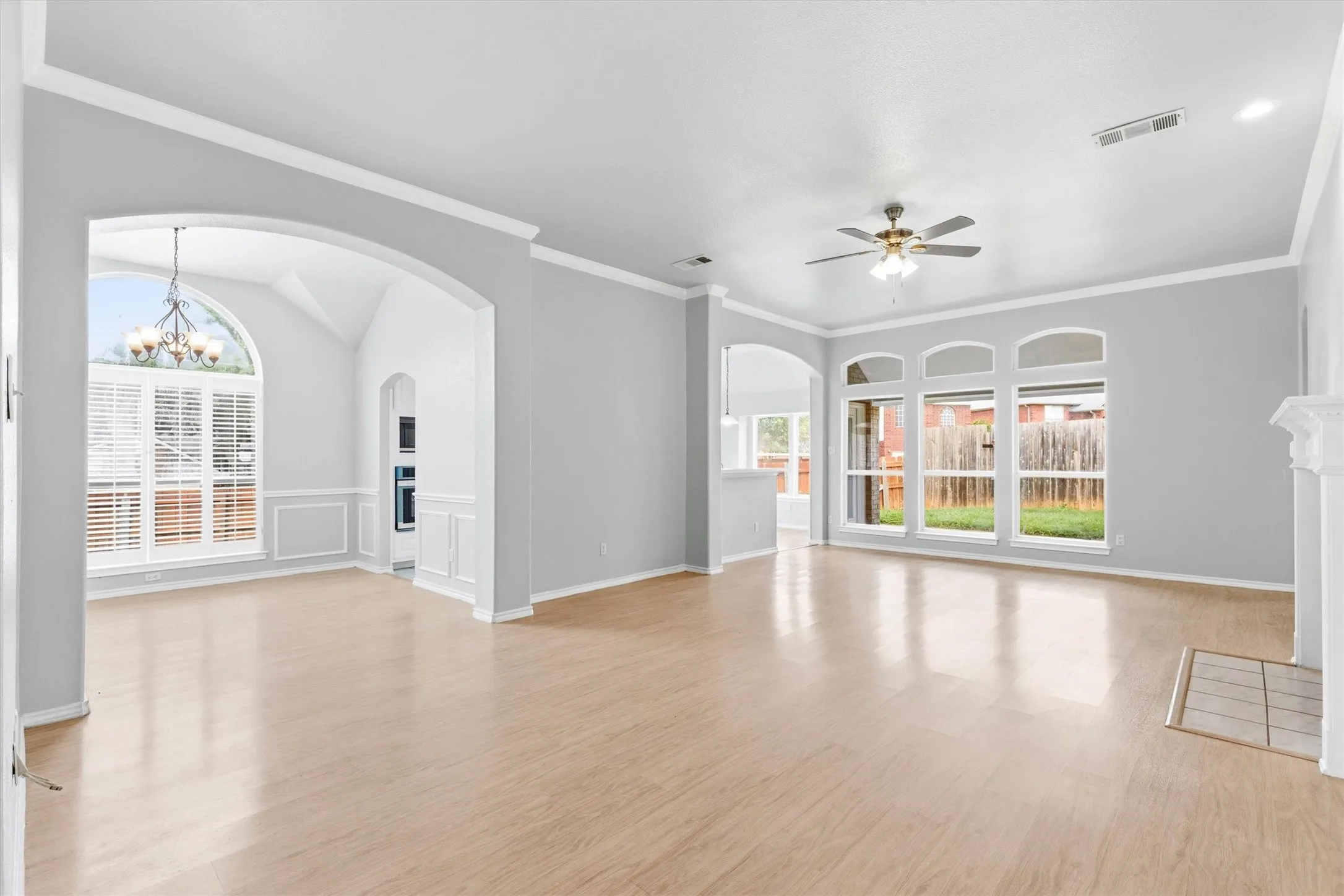 Spacious living area featuring light wood-finish flooring, multiple arched windows, and a ceiling fan