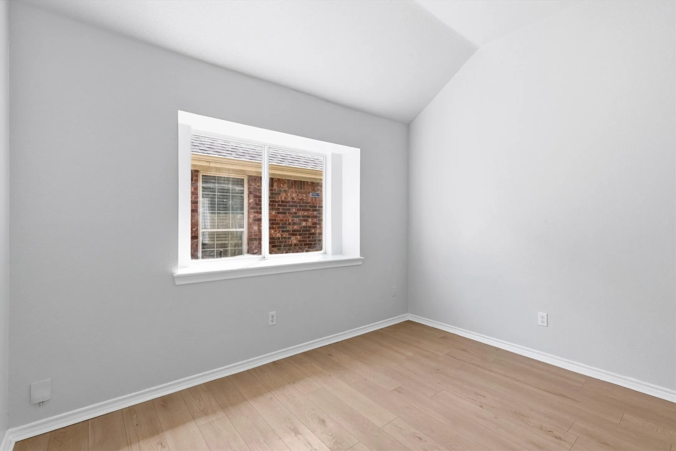 Room featuring light wood-finish flooring, crisp white baseboards, and a white framed window