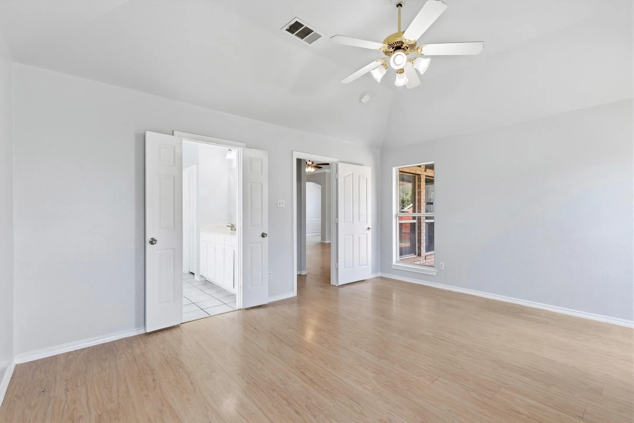 Spacious room featuring vaulted ceilings, wood-finish flooring, and a multi-blade ceiling fan