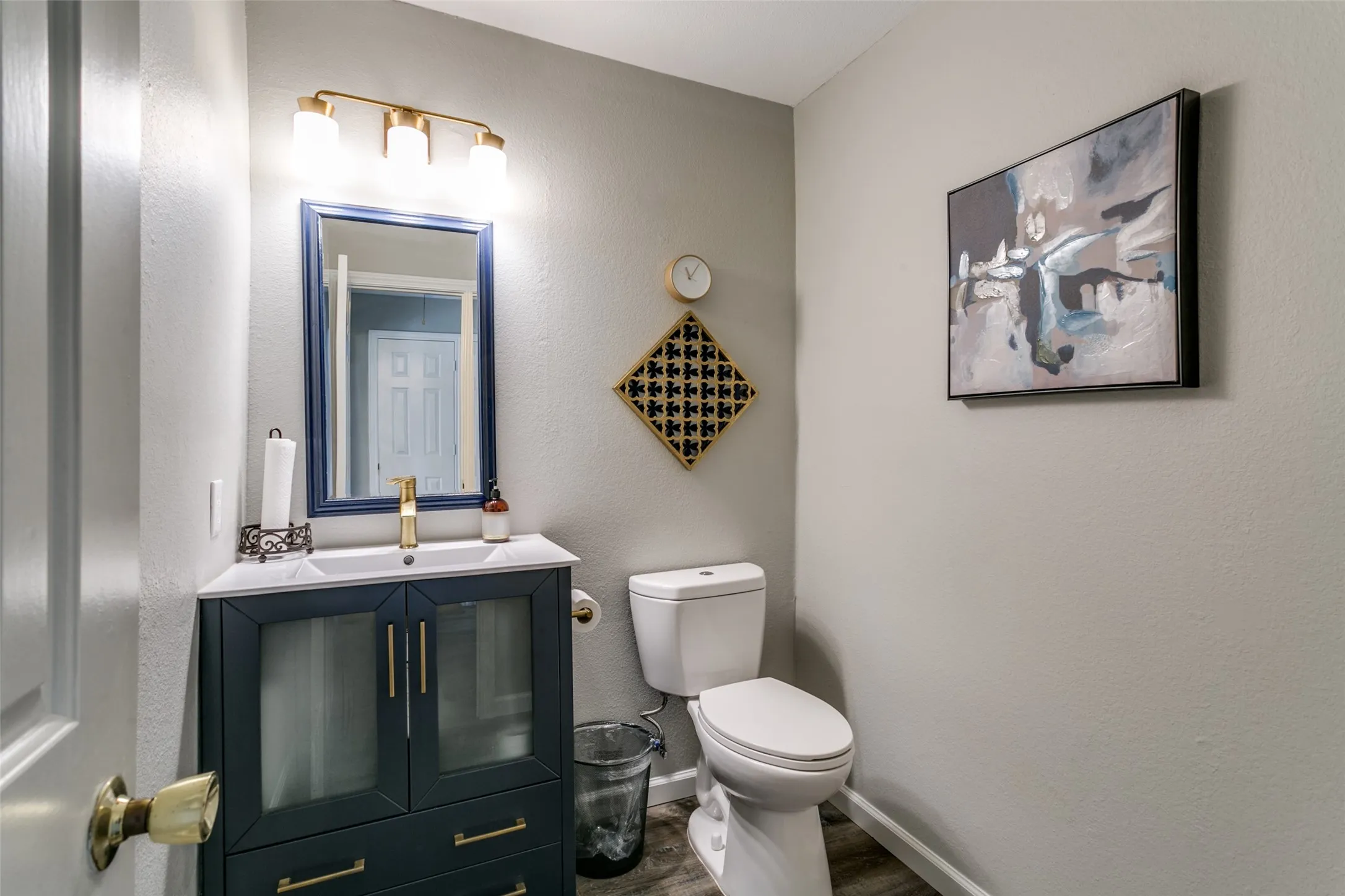 Powder room featuring a navy vanity with gold hardware, a white countertop, and a rectangular sink with a gold-tone faucet