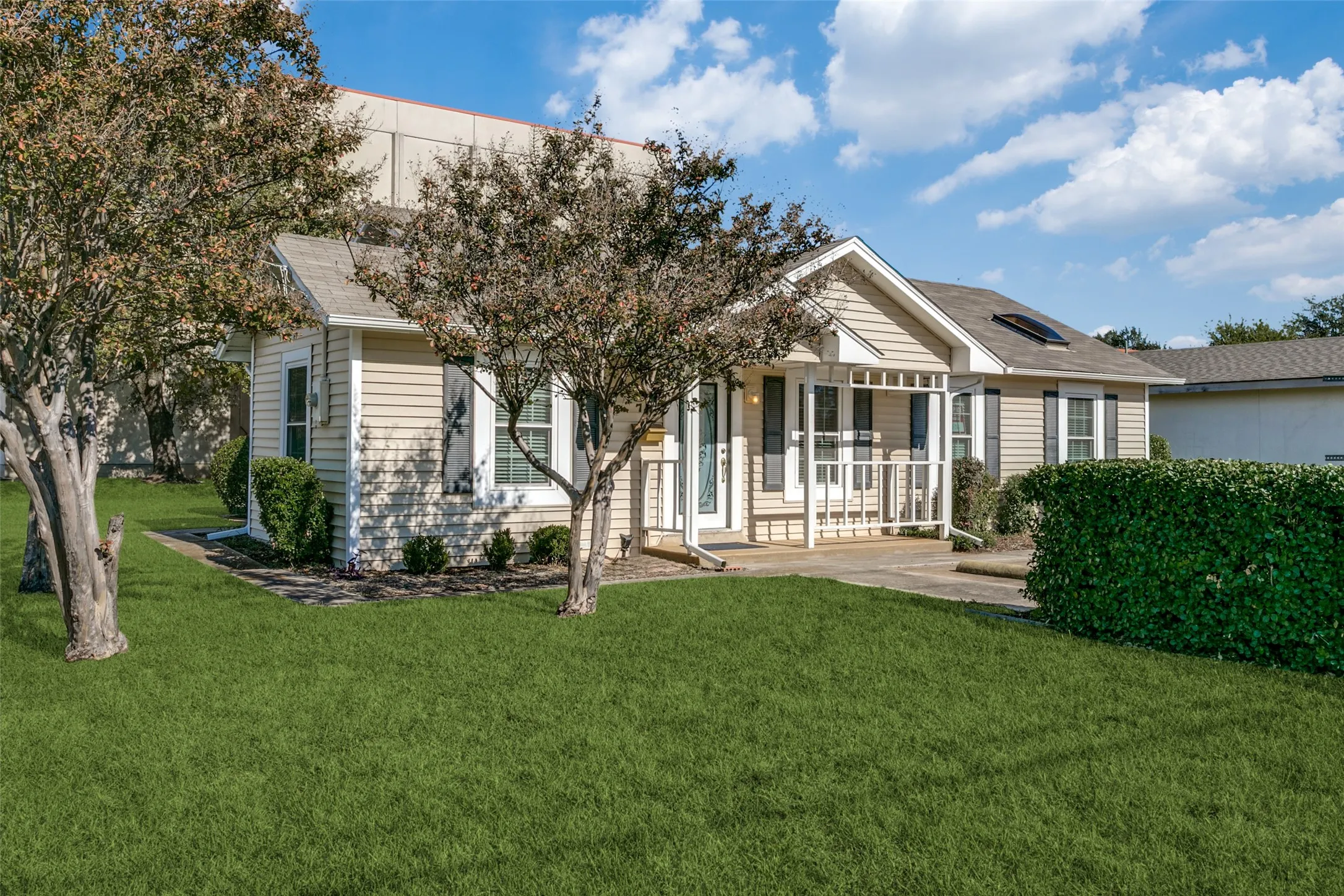 Charming single-story residence featuring light-colored siding, a covered front porch, and mature landscaping