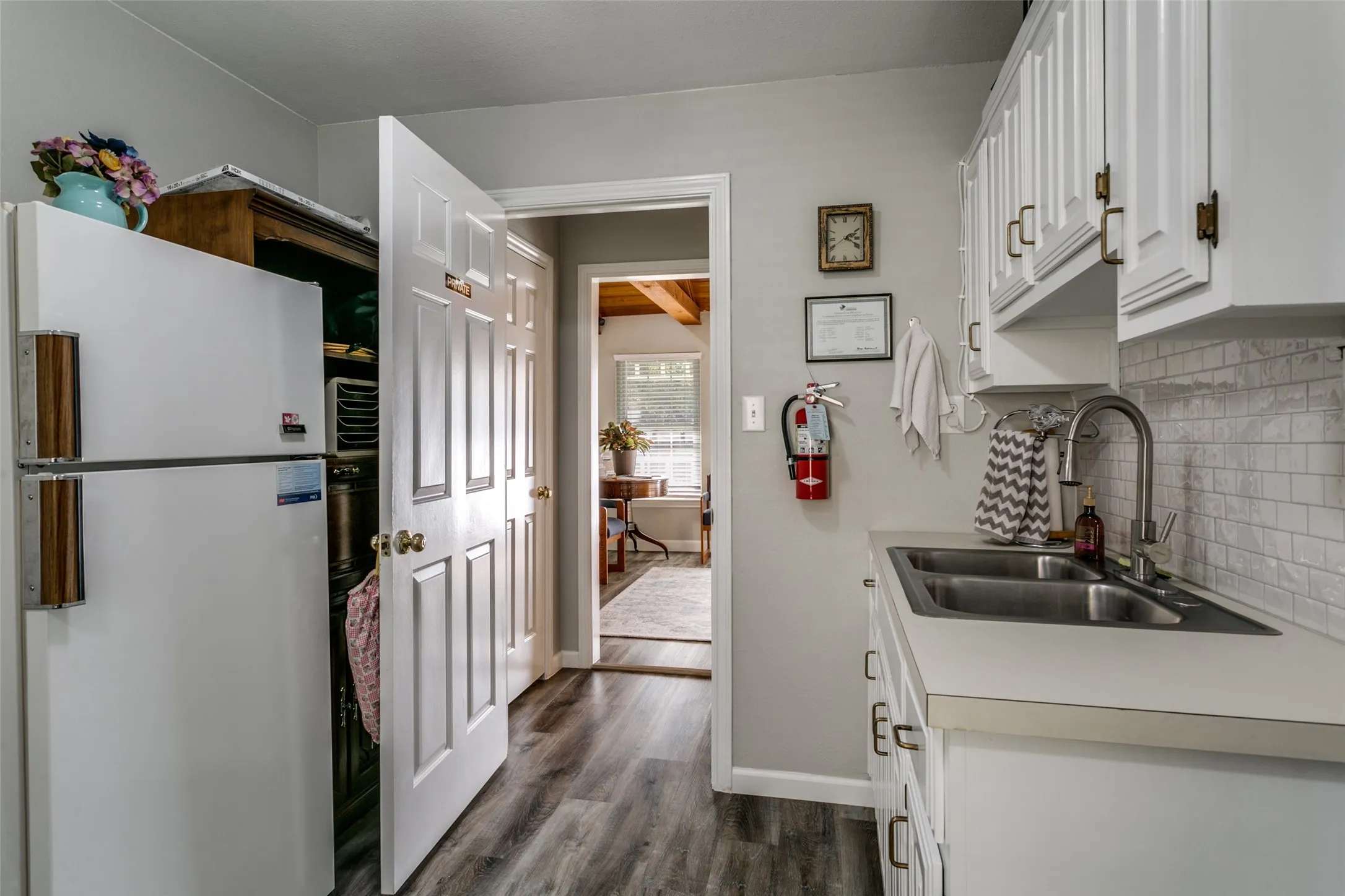 Kitchenette featuring wood-finish flooring, white cabinetry with gold-toned hardware, a double basin stainless steel sink with a high-arch faucet, and a light-toned countertop