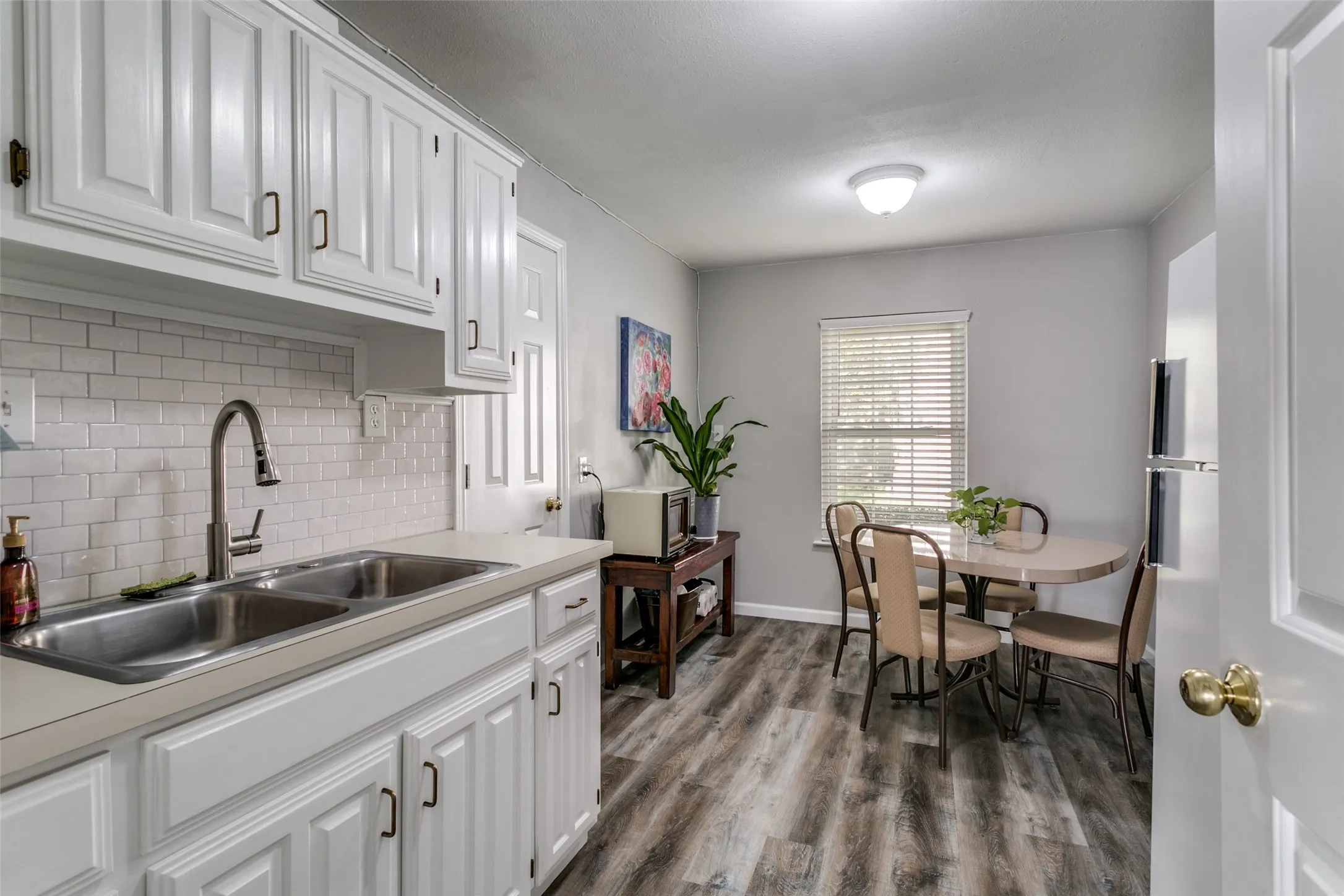 Kitchen featuring white cabinetry with dark hardware, a stainless steel double basin sink with a high-arc faucet, and a white subway tile backsplash