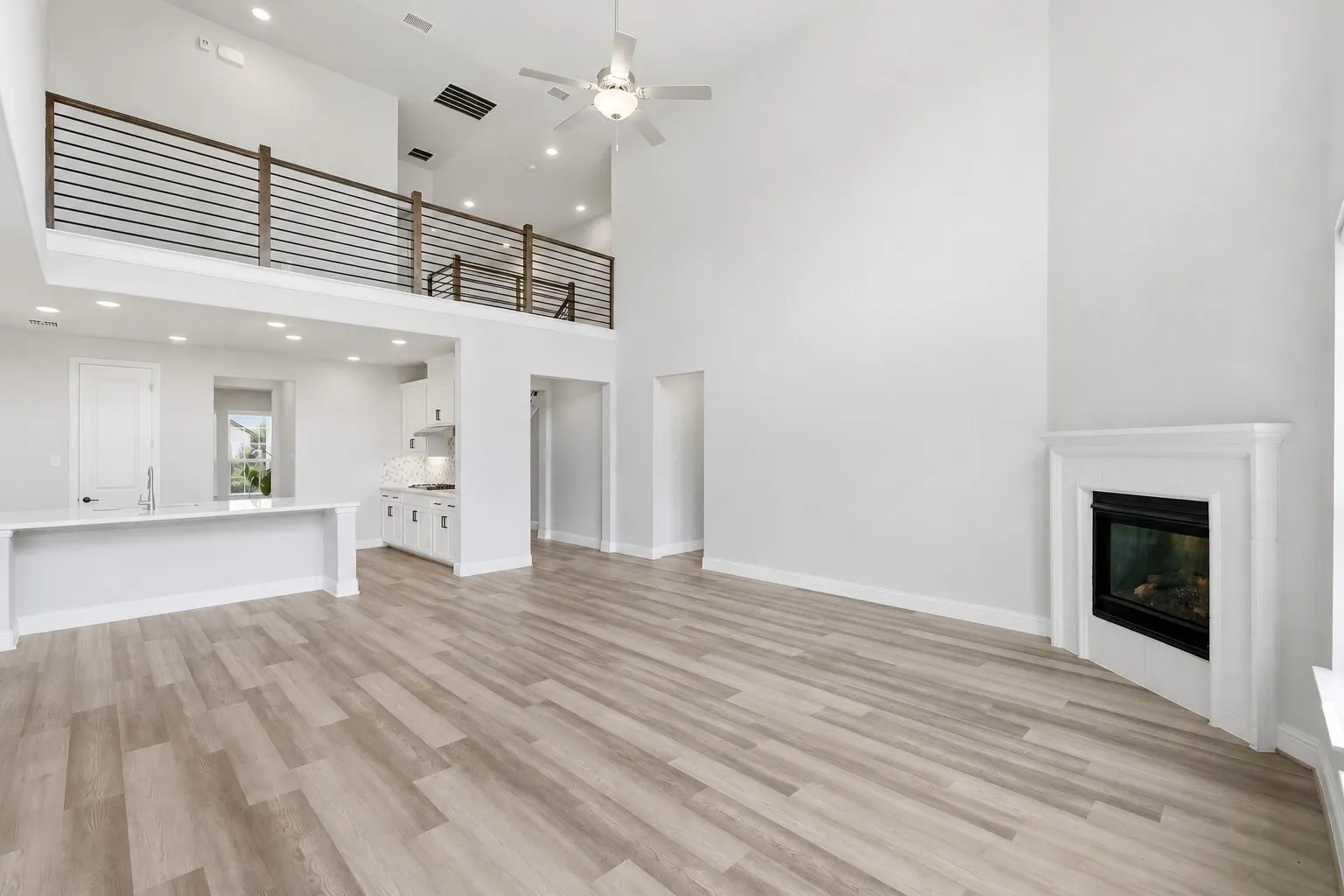Open-concept living area featuring high vaulted ceilings, light wood-finish flooring, a built-in fireplace with a white mantel, and a kitchen island with a sink