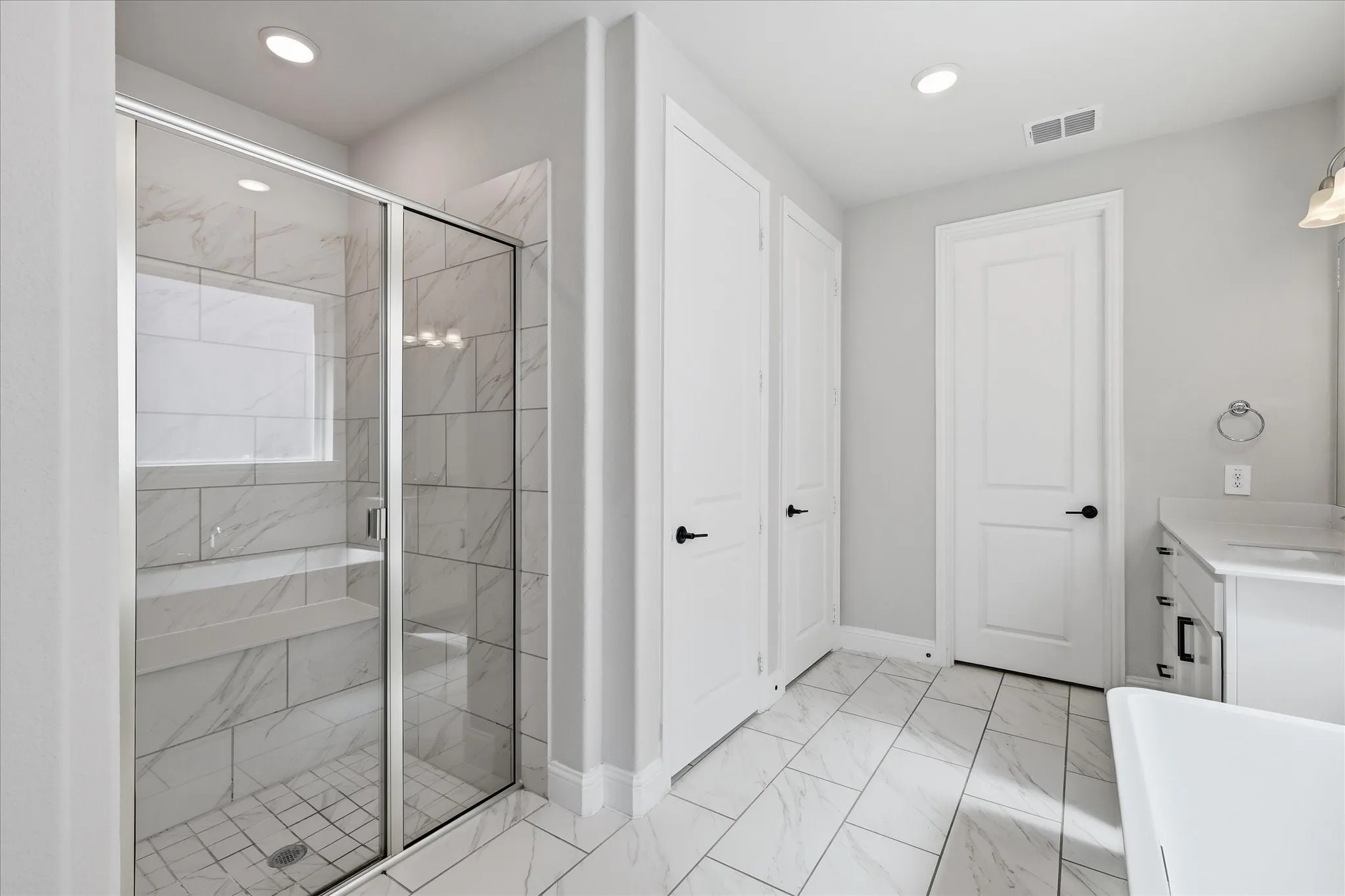 Spacious bathroom featuring a glass-enclosed shower with white marble-look tile, integrated bench, and a privacy window