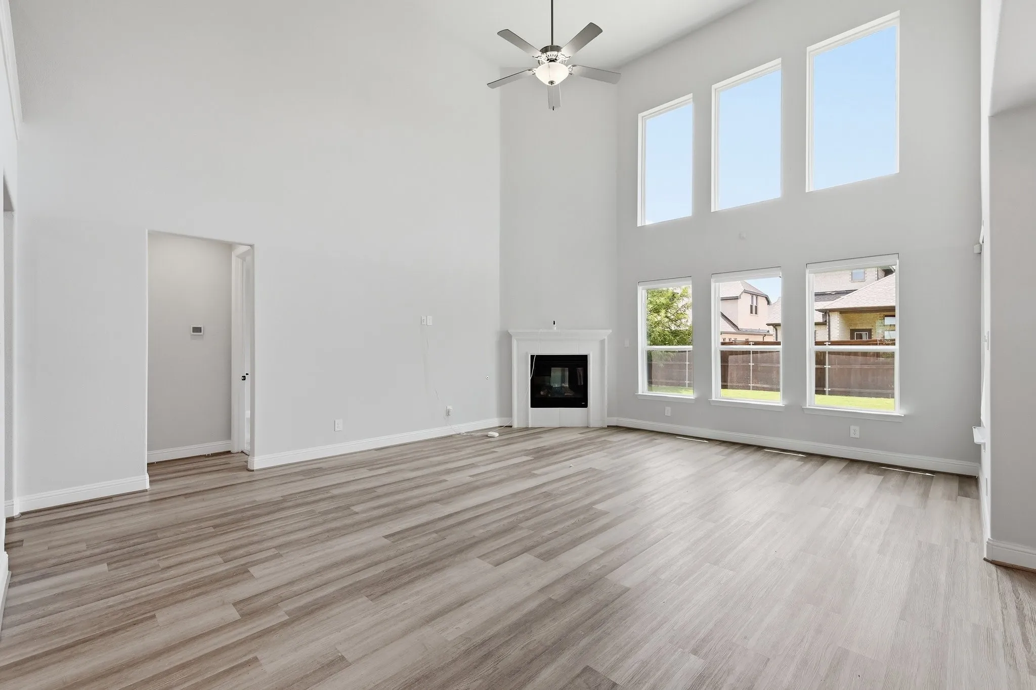 Spacious living area featuring high vaulted ceilings, expansive windows, a decorative fireplace with a mantel, wood-finish flooring, and a ceiling fan