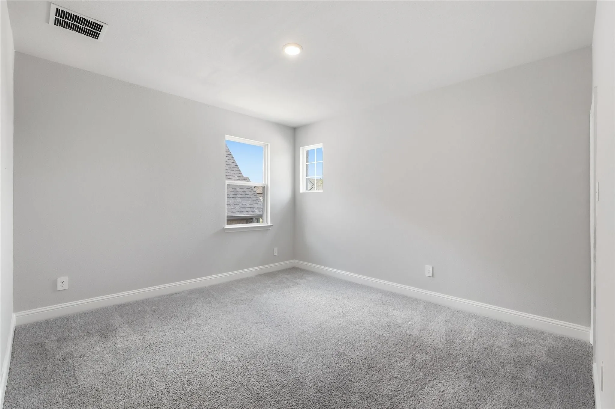 Spacious room featuring light gray walls, gray carpet flooring, white trim, and a recessed ceiling light