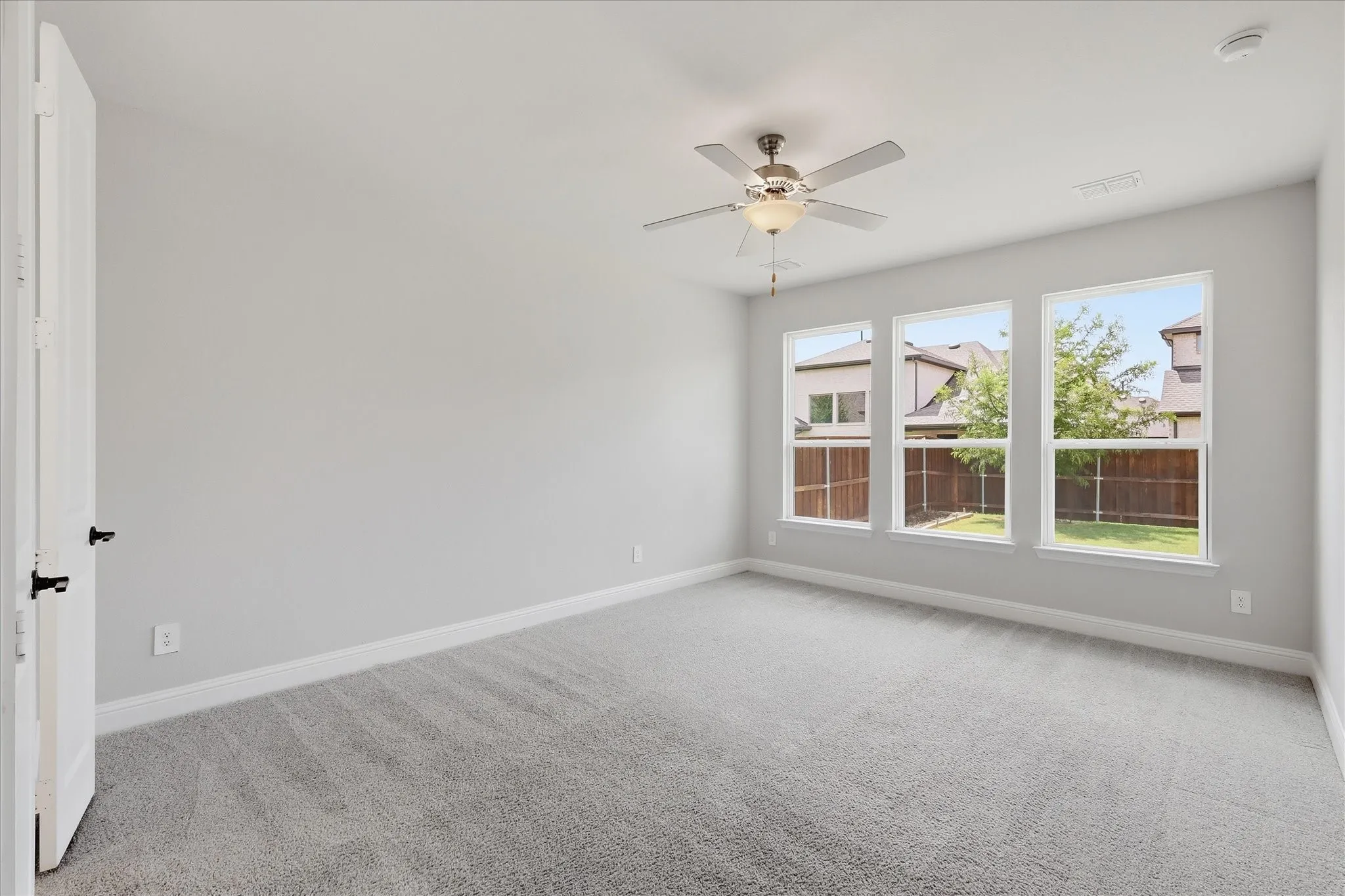 Bright room featuring three large windows, light gray carpet, and a ceiling fan with integrated lighting