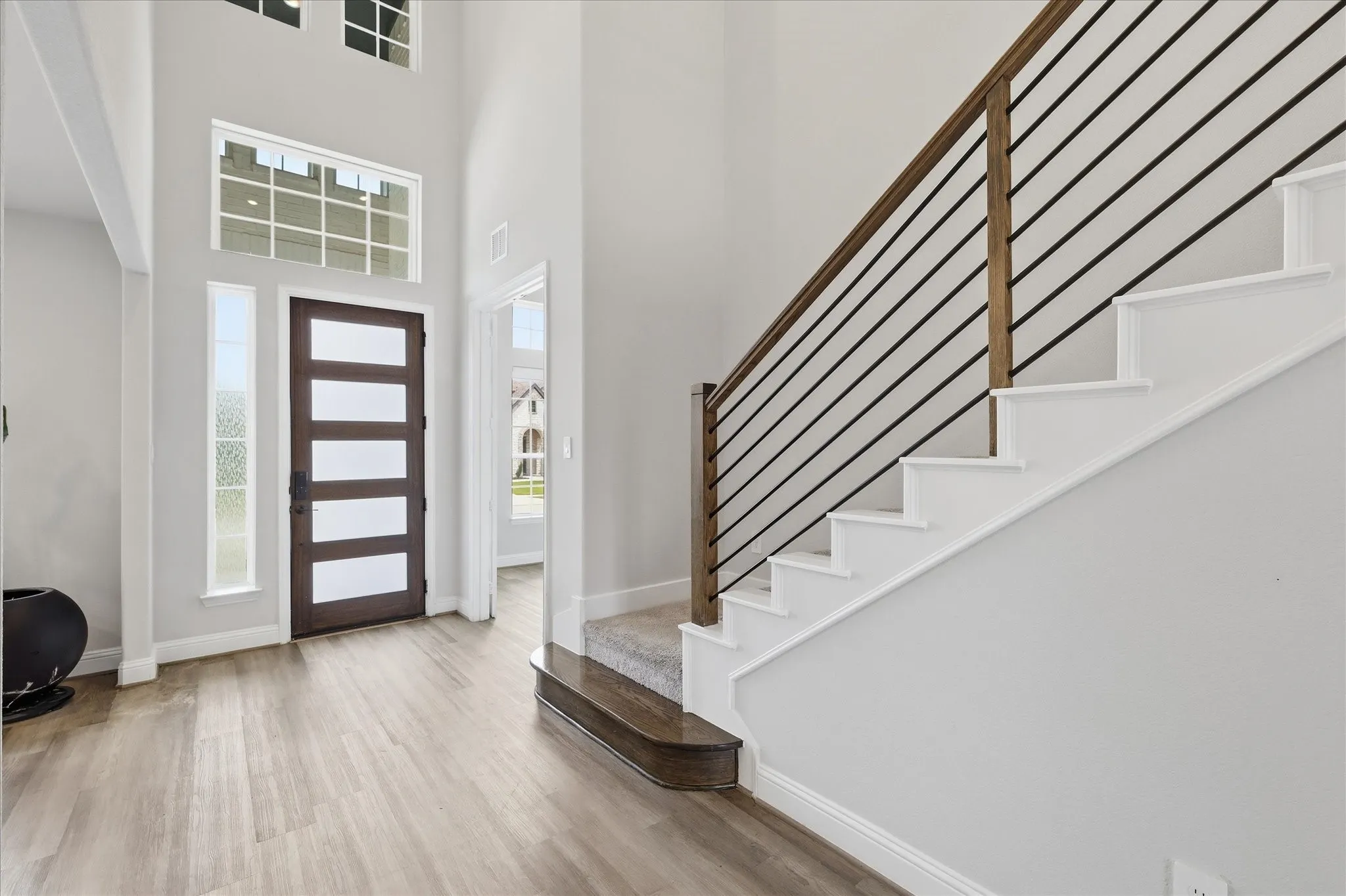 Grand entryway featuring a soaring ceiling, wood-finish flooring, a modern five-panel glass door, and a staircase with a horizontal metal railing and wood handrail