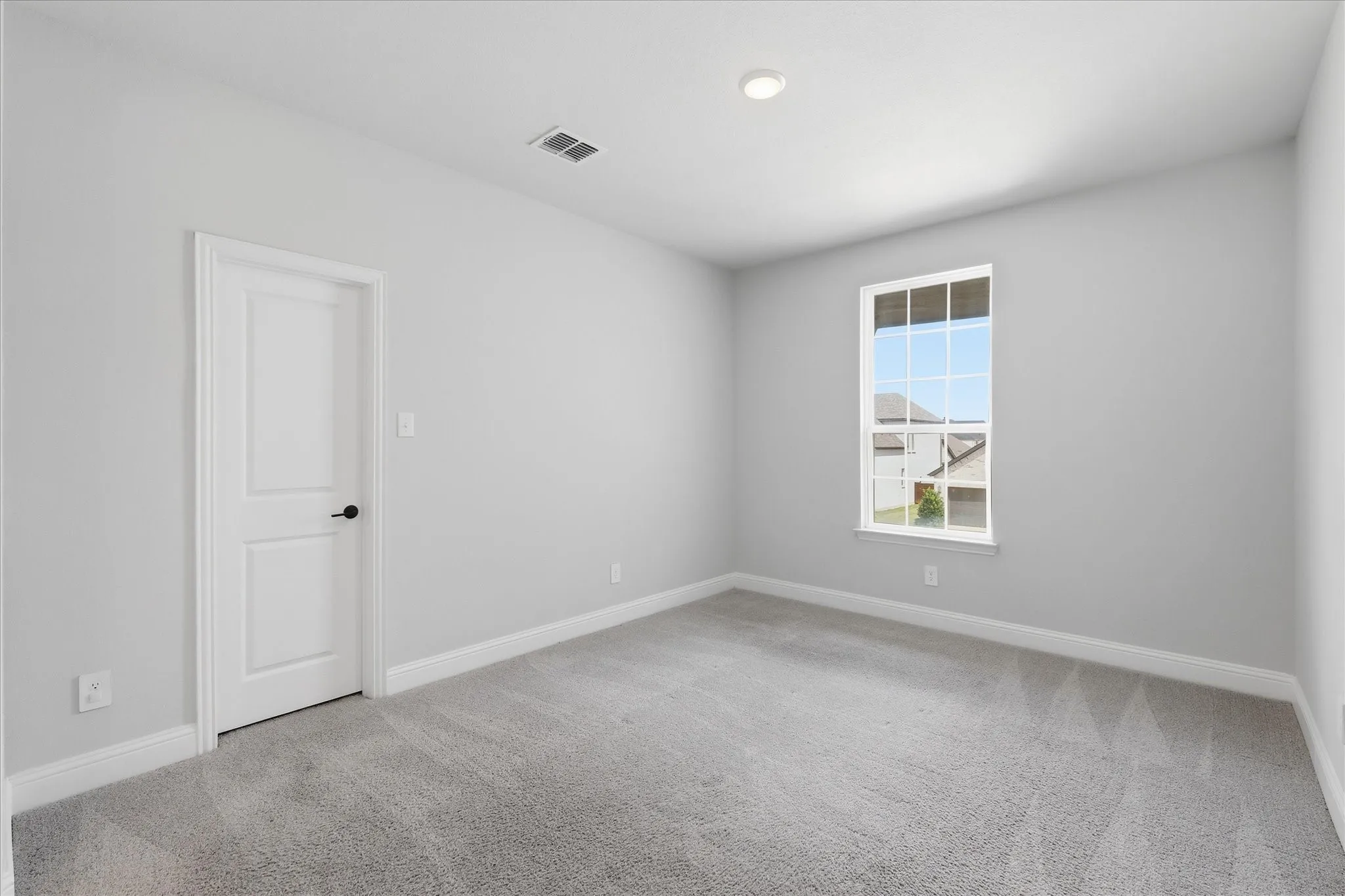 Neutral-toned room featuring light gray walls, gray carpet flooring, white baseboards, and a white interior door with black hardware