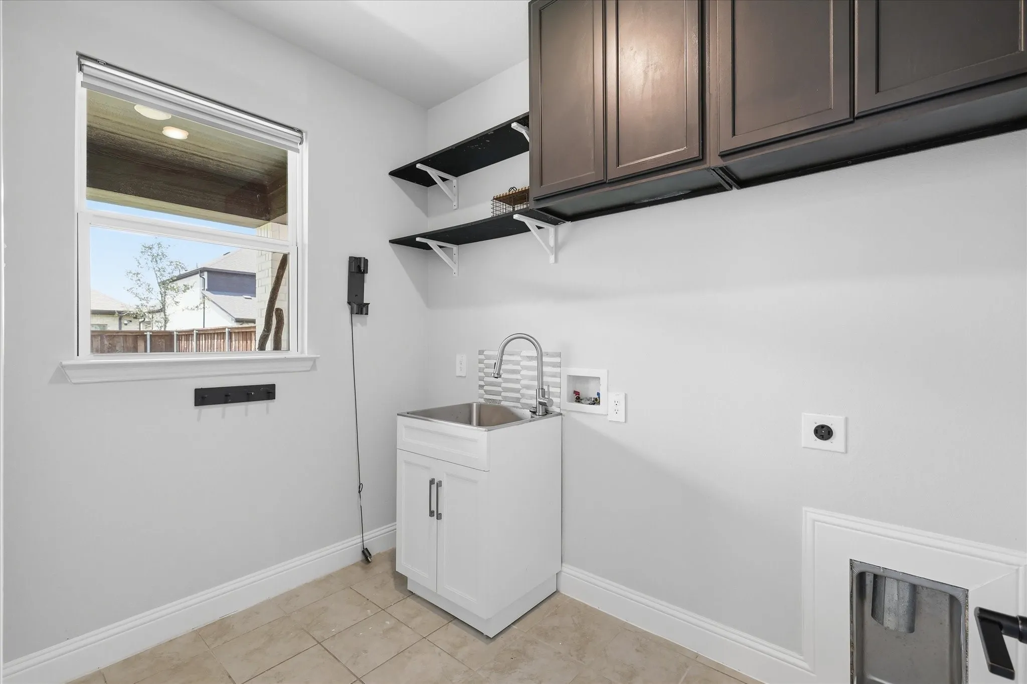Laundry room featuring ceramic tile flooring, a utility sink with a tiled backsplash, dark wood-finish upper cabinetry, and open shelving