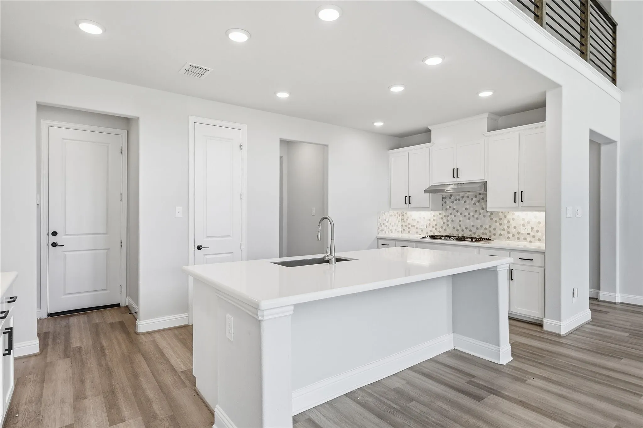 Modern kitchen featuring an expansive island with an undermount sink, white cabinetry with dark hardware, a mosaic tile backsplash, stainless steel range hood, and wood-finish flooring
