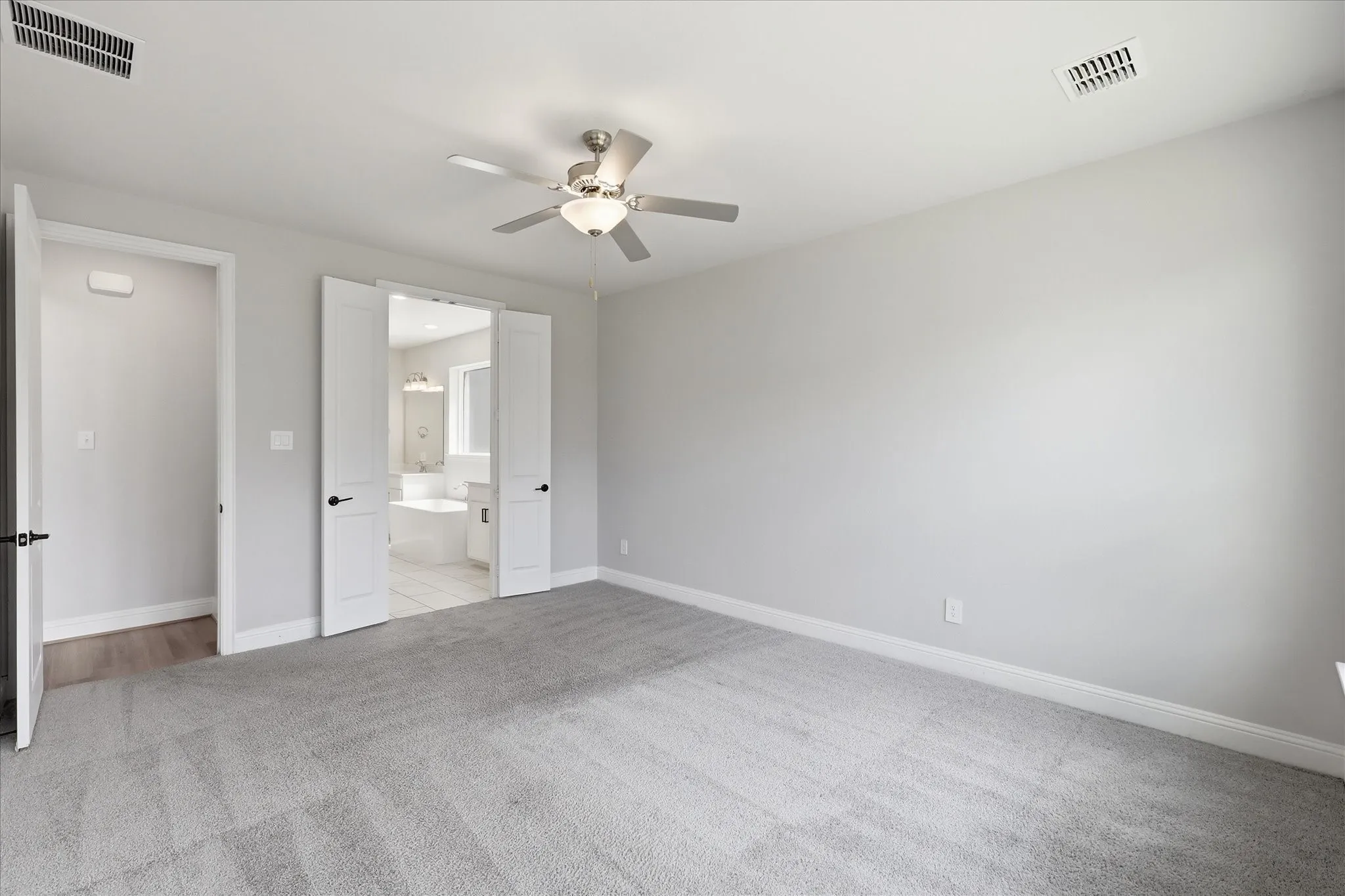 Carpeted room featuring a ceiling fan with integrated lighting, light gray wall paint, white trim, and white paneled doors opening to a bathroom with a white soaking tub and tile flooring