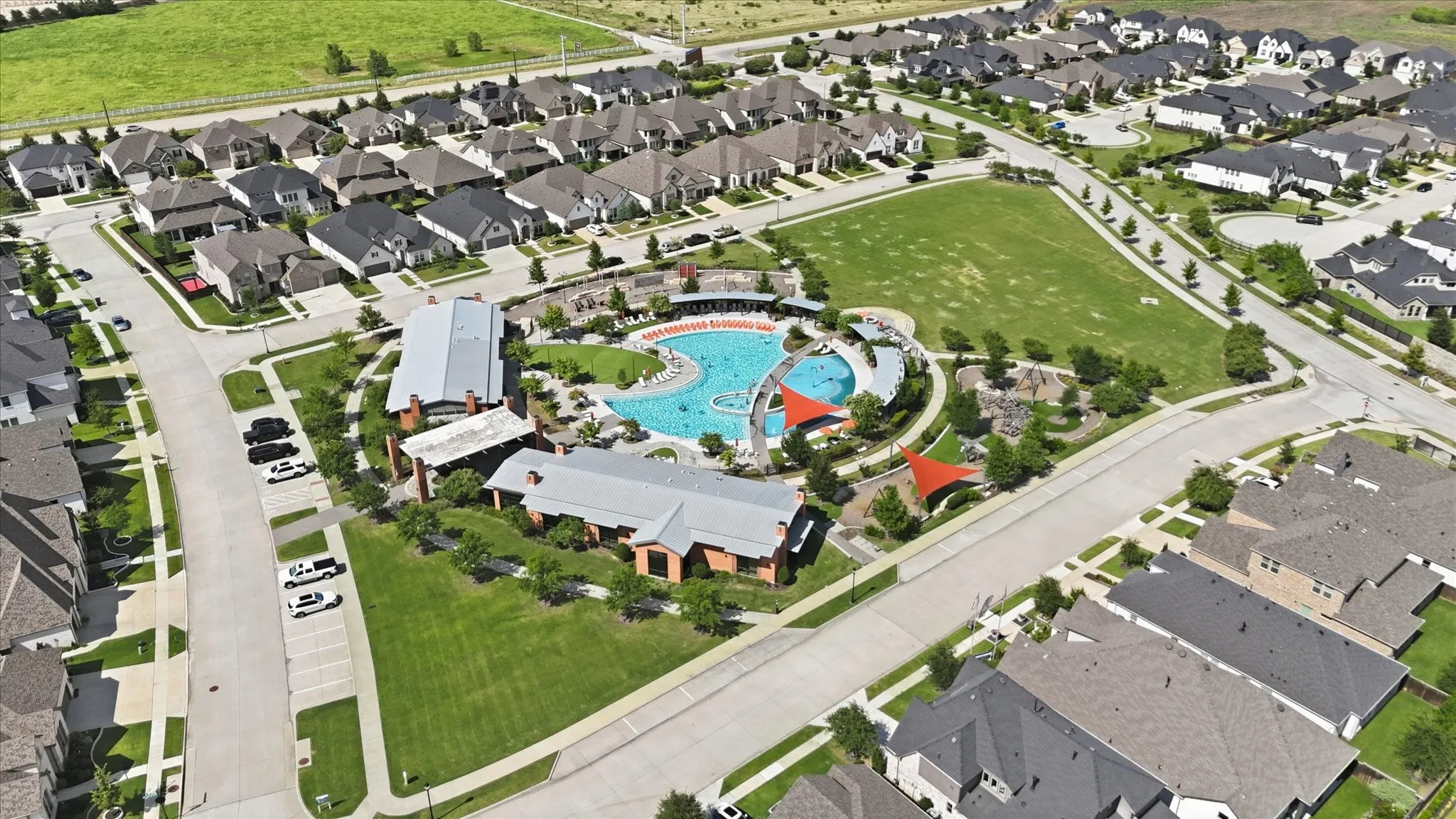 Aerial view of a residential community featuring a large aquatic center, expansive green space, and a collection of single-family homes