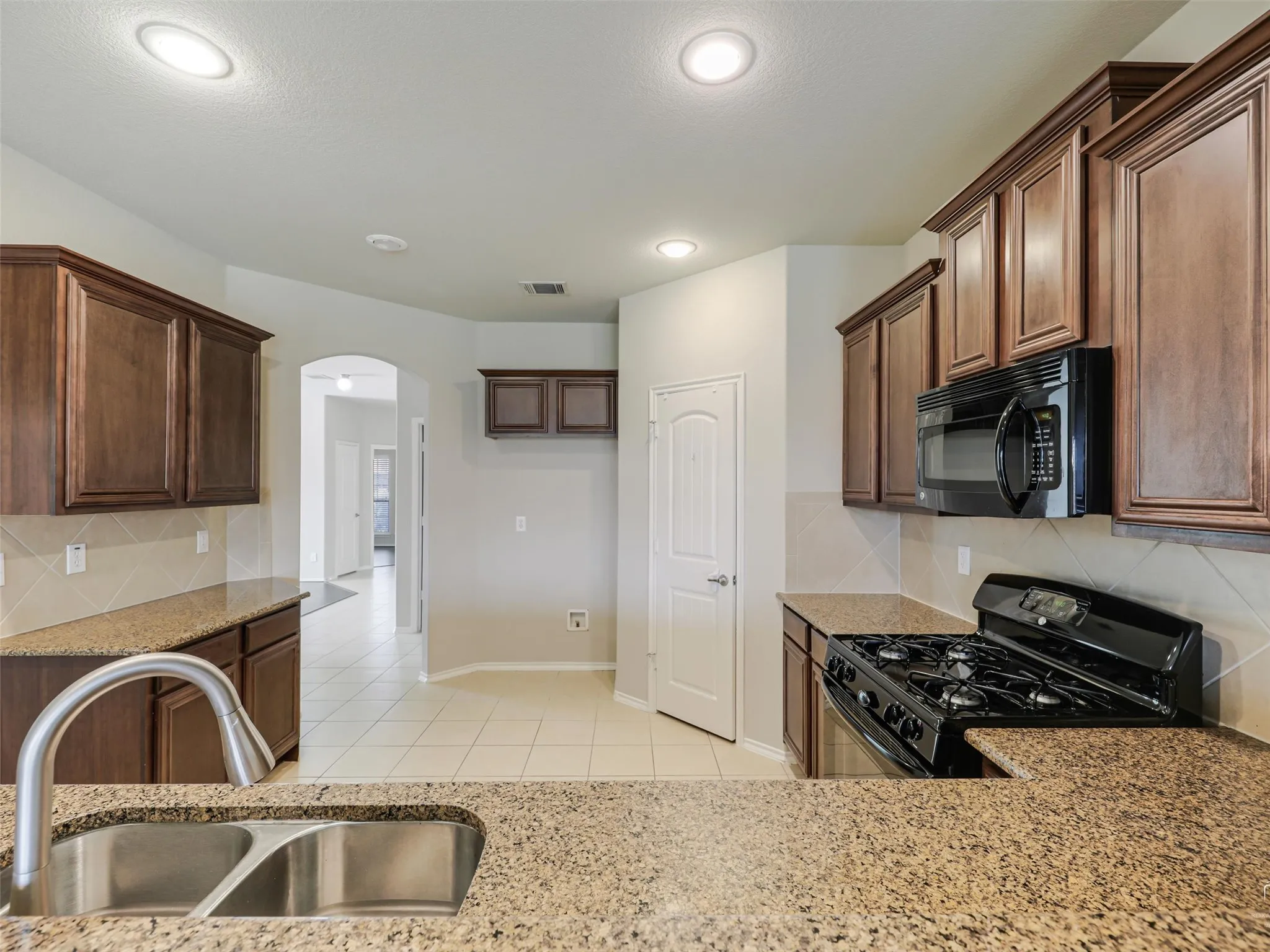 Kitchen featuring recessed lighting, dark wood cabinetry, light speckled countertops, a tile backsplash, and a double basin stainless steel sink with a high-arc faucet