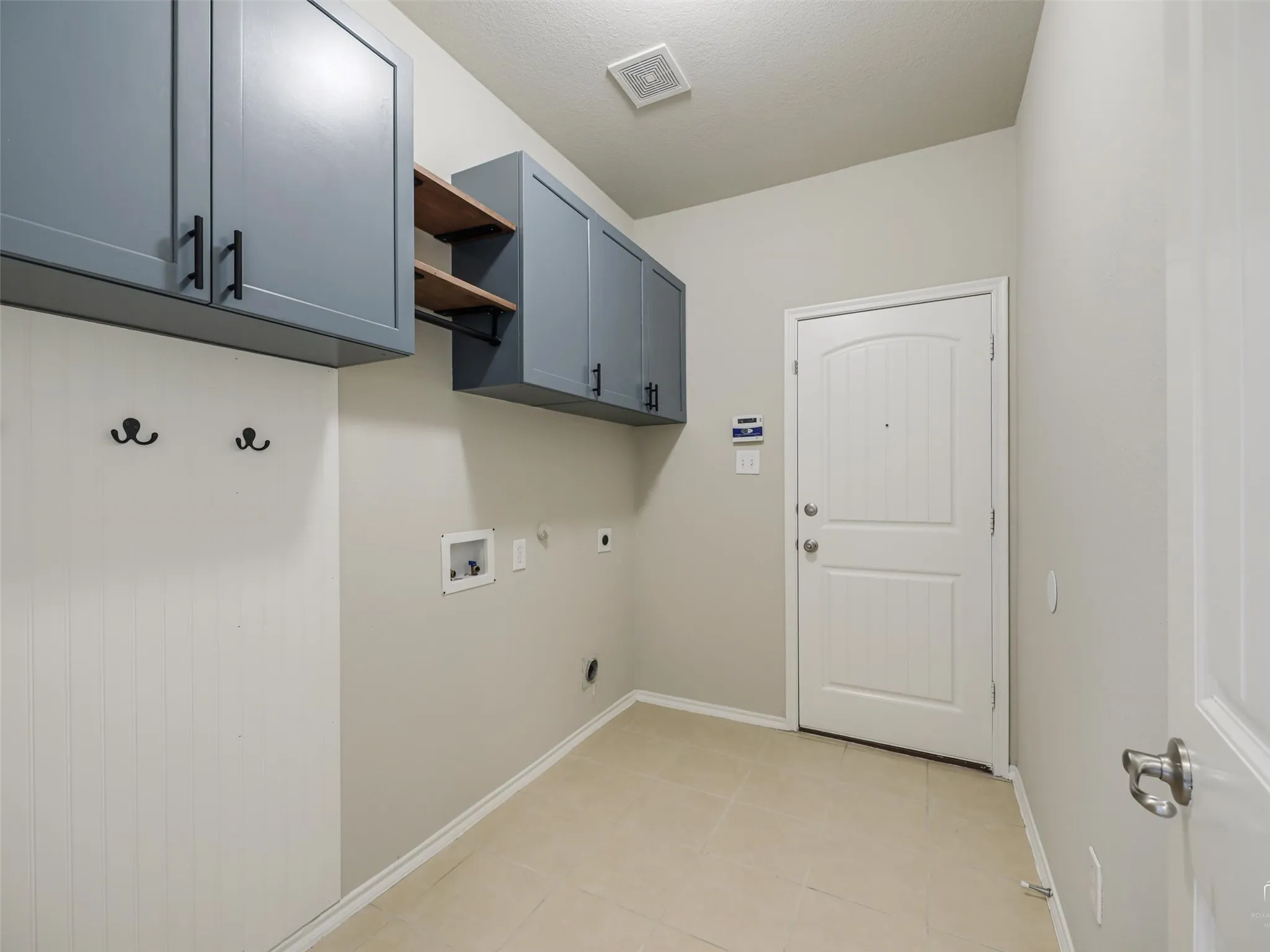 Utility space featuring gray cabinetry, wood-finish shelving, and ceramic tile flooring