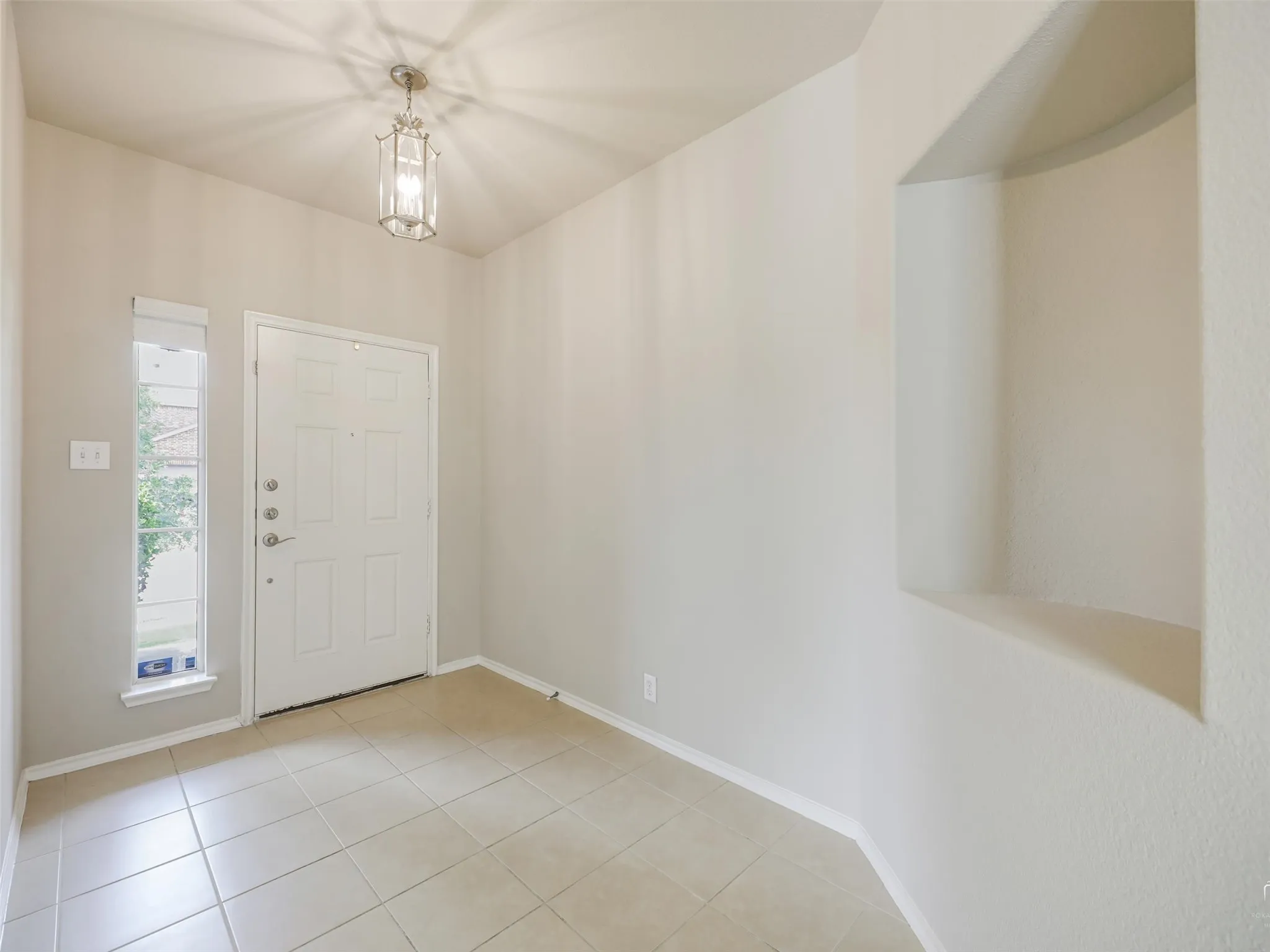 Foyer featuring neutral-toned tile flooring, a recessed wall niche, and a white front door with a side window