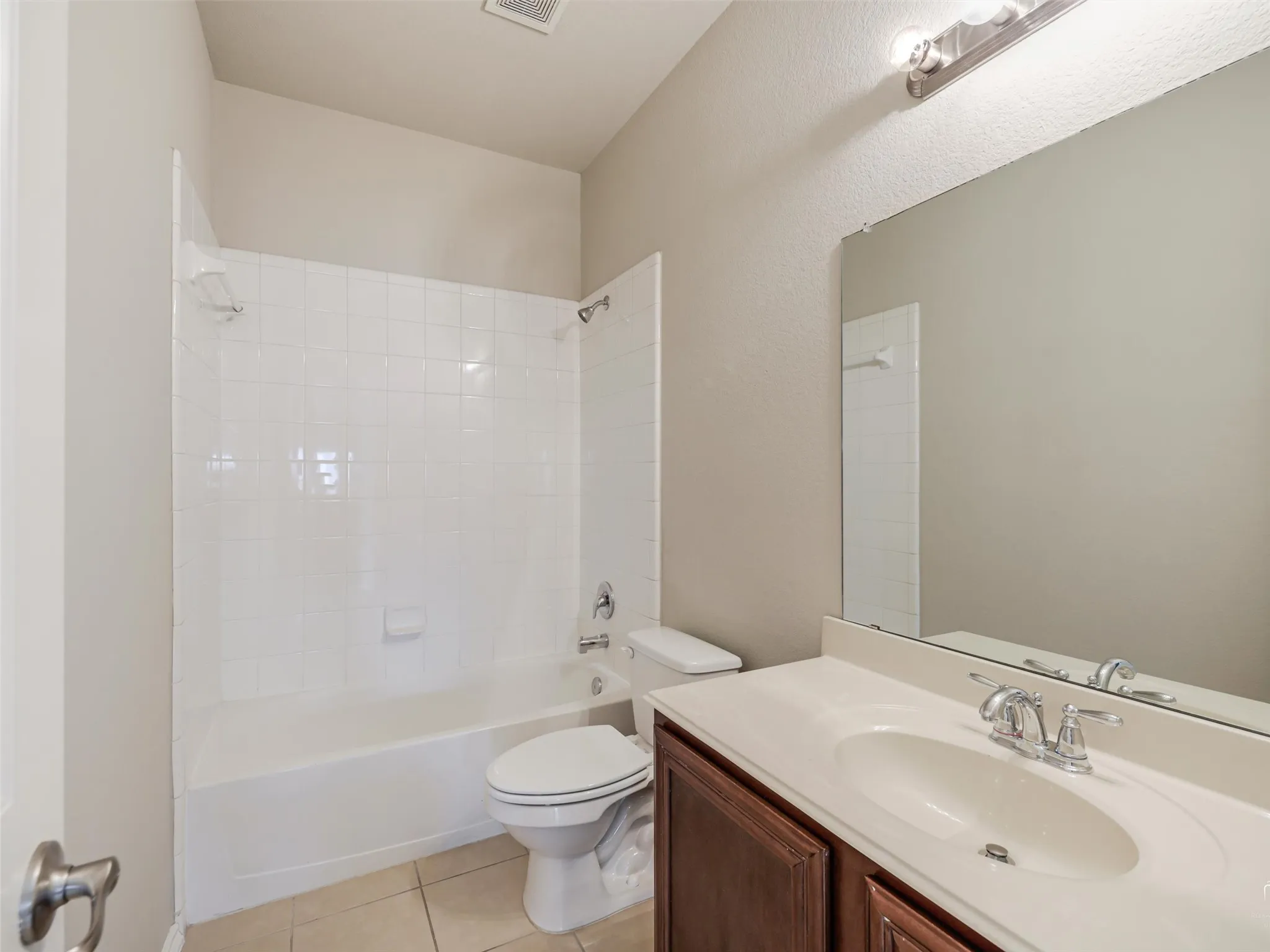 Full bathroom featuring a white tub with shower, white tile surround, a dark wood-finish vanity with an integrated sink, and an overhead vanity light fixture