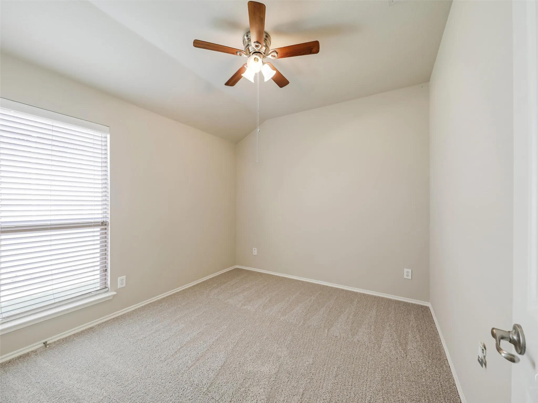 Carpeted room featuring a ceiling fan with light fixture, vaulted ceiling, neutral wall color, and window with blinds