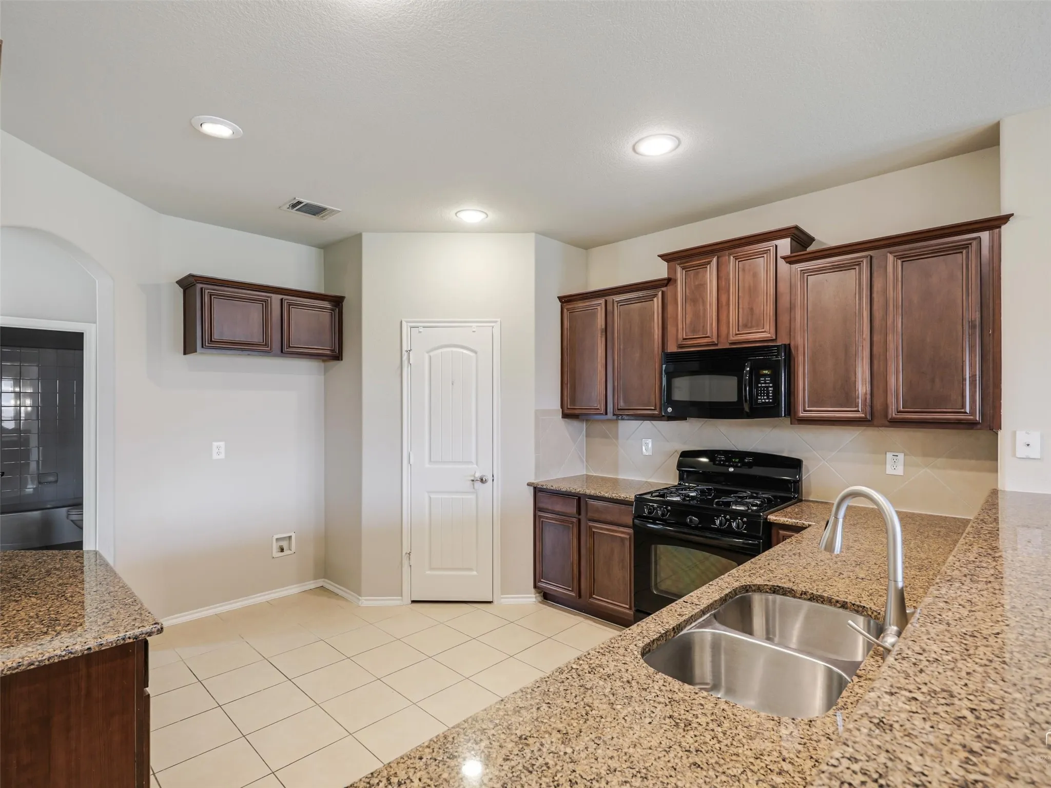 Kitchen featuring granite countertops, wood cabinetry, tile backsplash, stainless steel double-basin sink, and recessed lighting