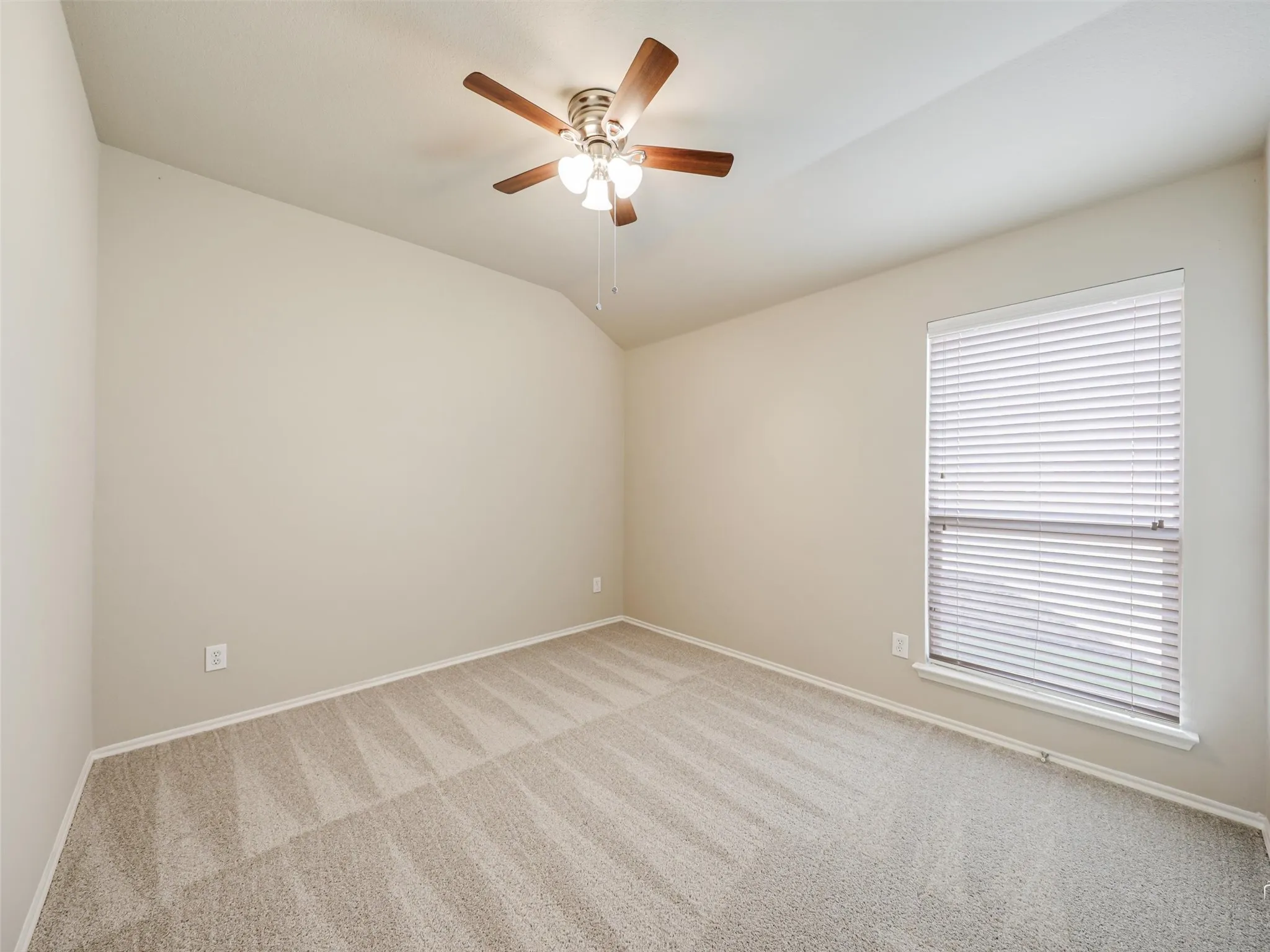 Carpeted room featuring a single window with horizontal blinds, neutral wall paint, white baseboards, and a ceiling fan with wood-finish blades and a four-light fixture