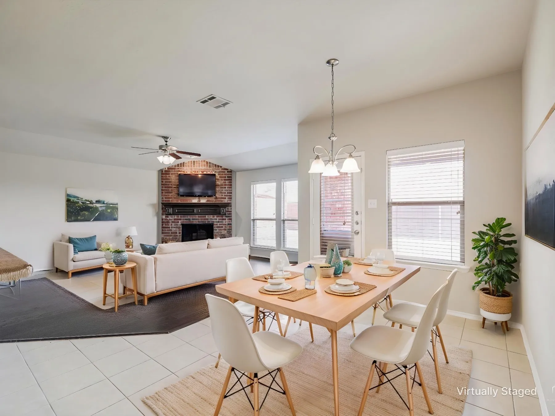 Virtually staged - Open-concept living and dining areas featuring a brick fireplace, a built-in ceiling fan, and multiple windows with blinds