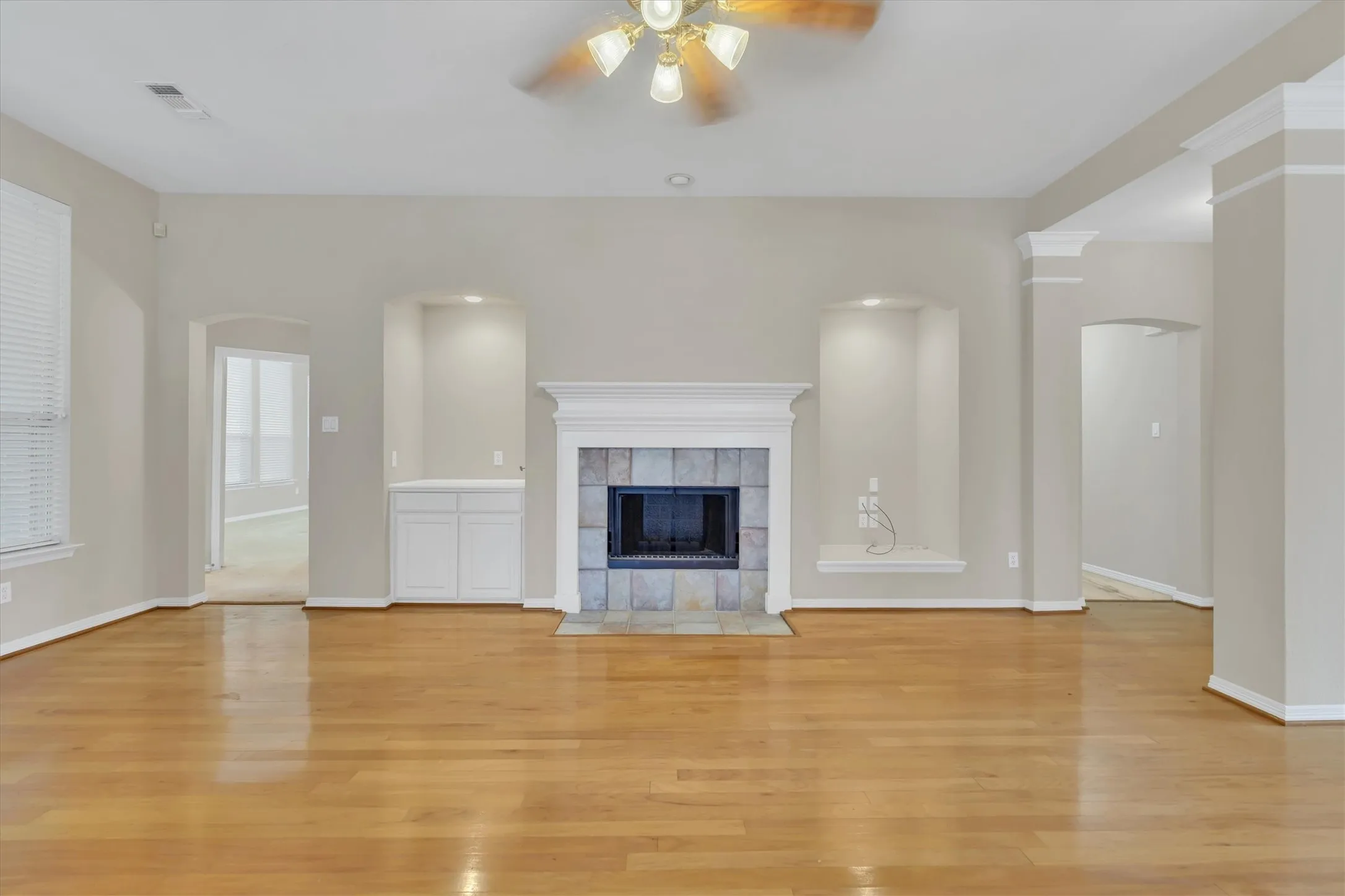Living area with wood-finish flooring, a fireplace featuring a tile surround and white mantel, built-in cabinetry, and recessed wall niches