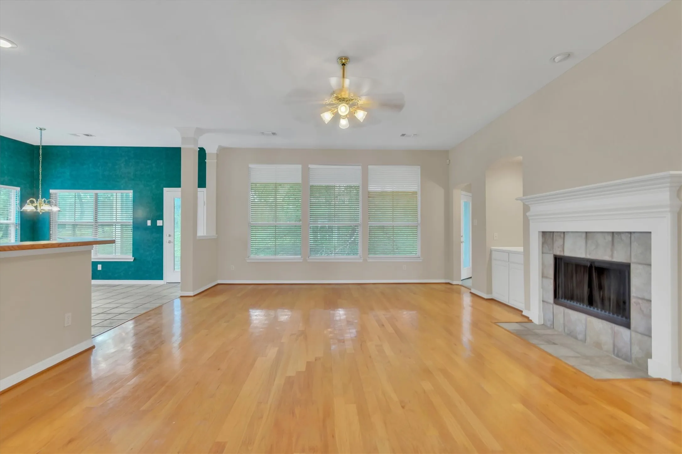 Spacious living area featuring polished wood-finish flooring, a ceiling fan with integrated lighting, and multiple windows