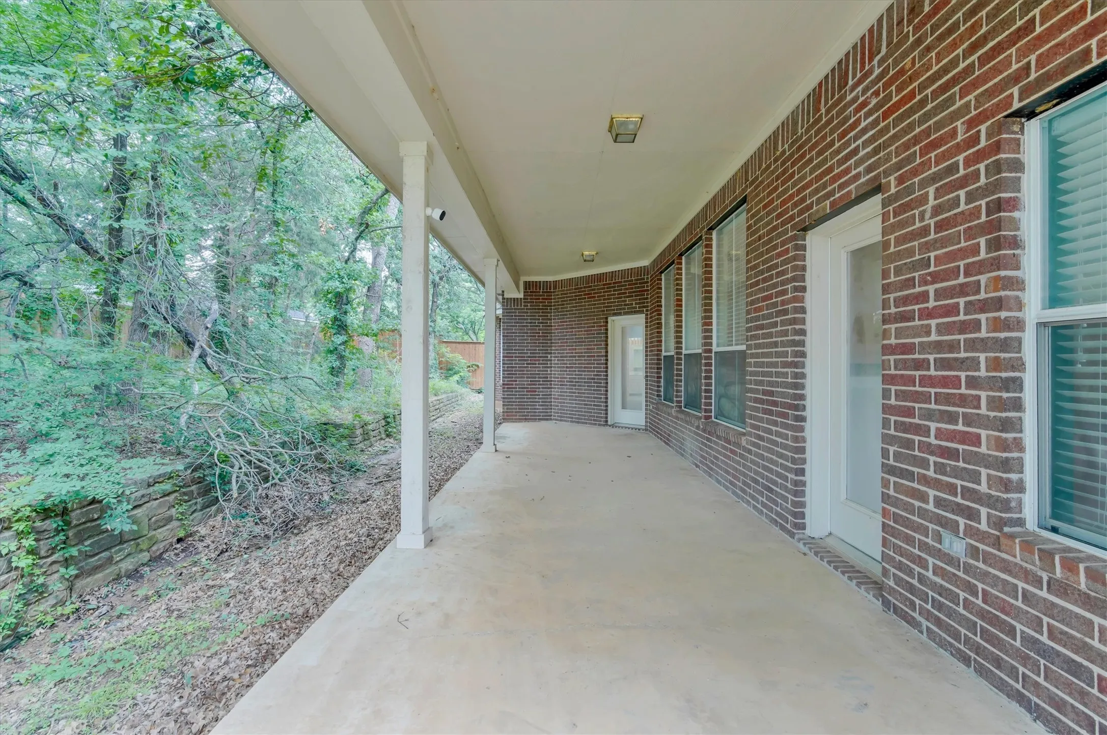 Back  Covered patio with a concrete surface and multiple access points, featuring a brick exterior and a stone retaining wall