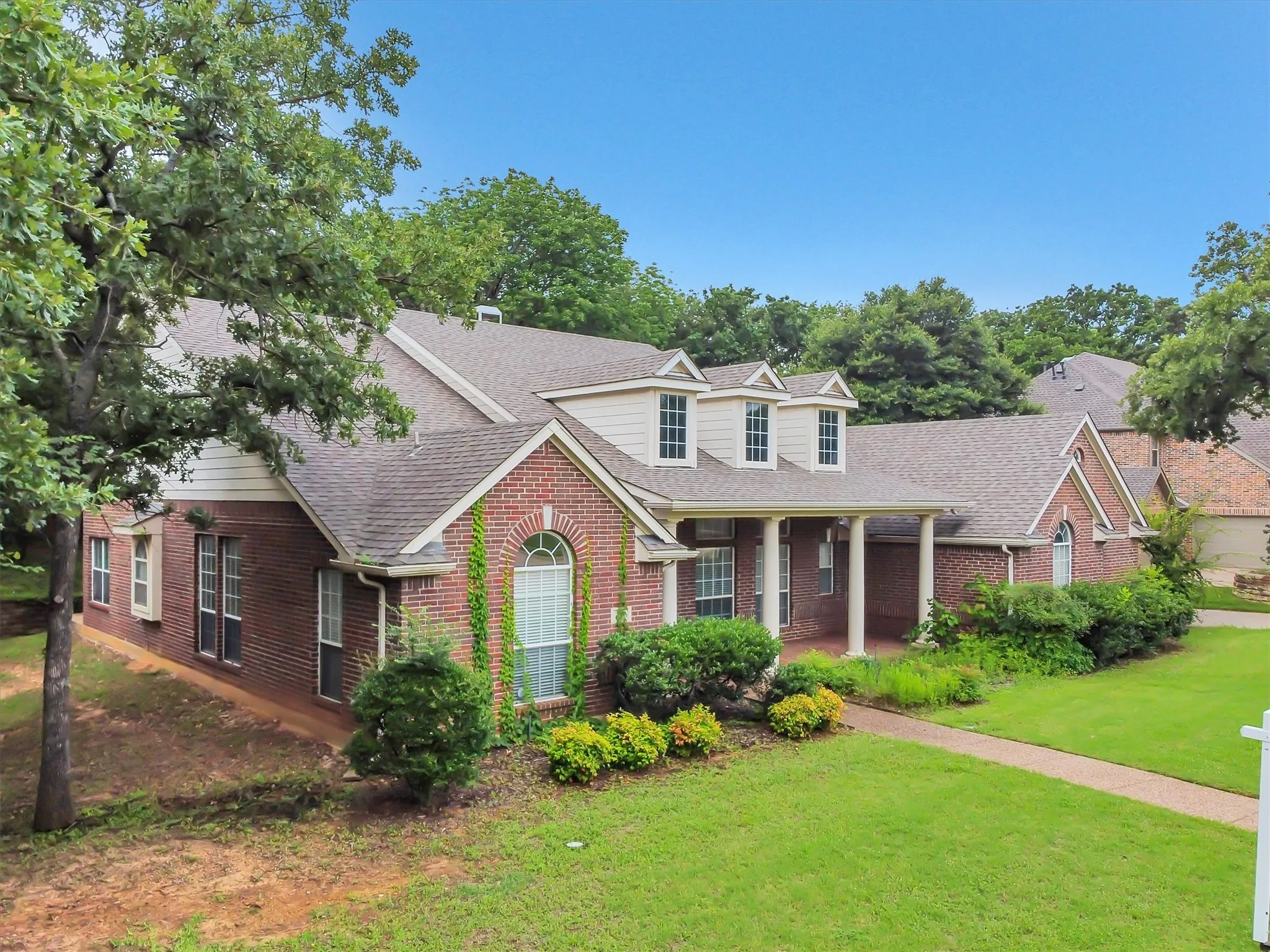 Brick exterior featuring an arched window, a gabled roofline, a concrete driveway, a wooden privacy fence, and a stone retaining wall