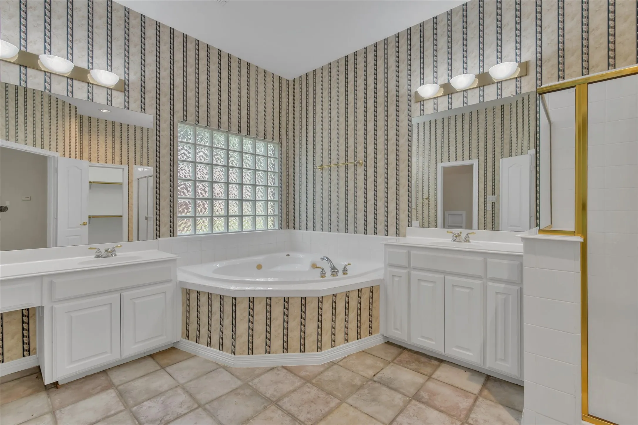 Primary Bathroom featuring a corner soaking tub, a glass block window, and dual vanities with integrated sinks