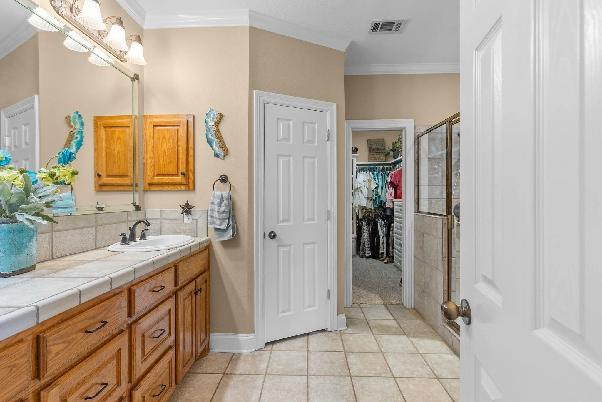 Bathroom vanity featuring a single basin sink set into a tile countertop, wood cabinetry, and a framed mirror
