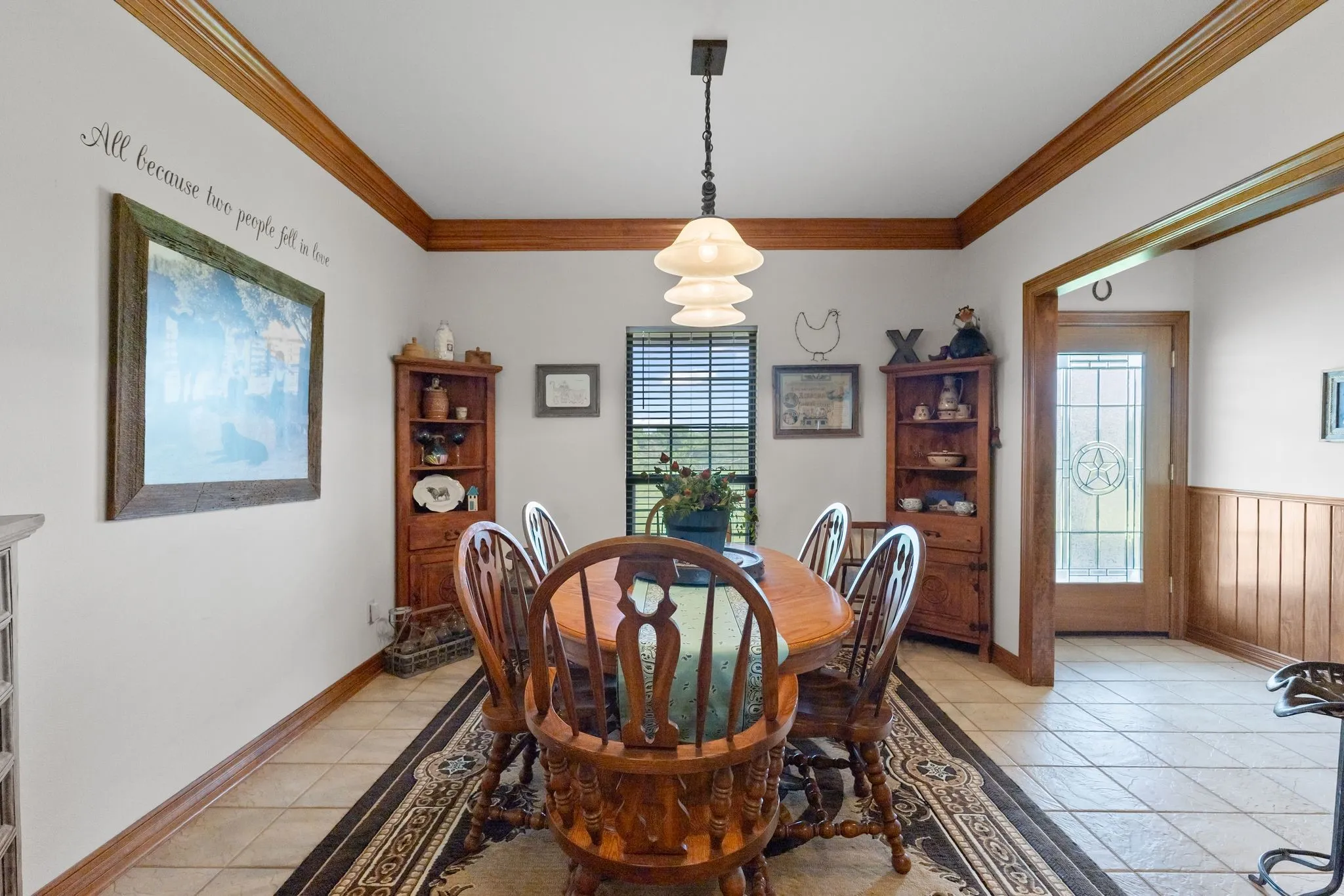 Dining area featuring tile flooring, wood-finish crown molding, wood-finish chair rail, and a decorative pendant light fixture