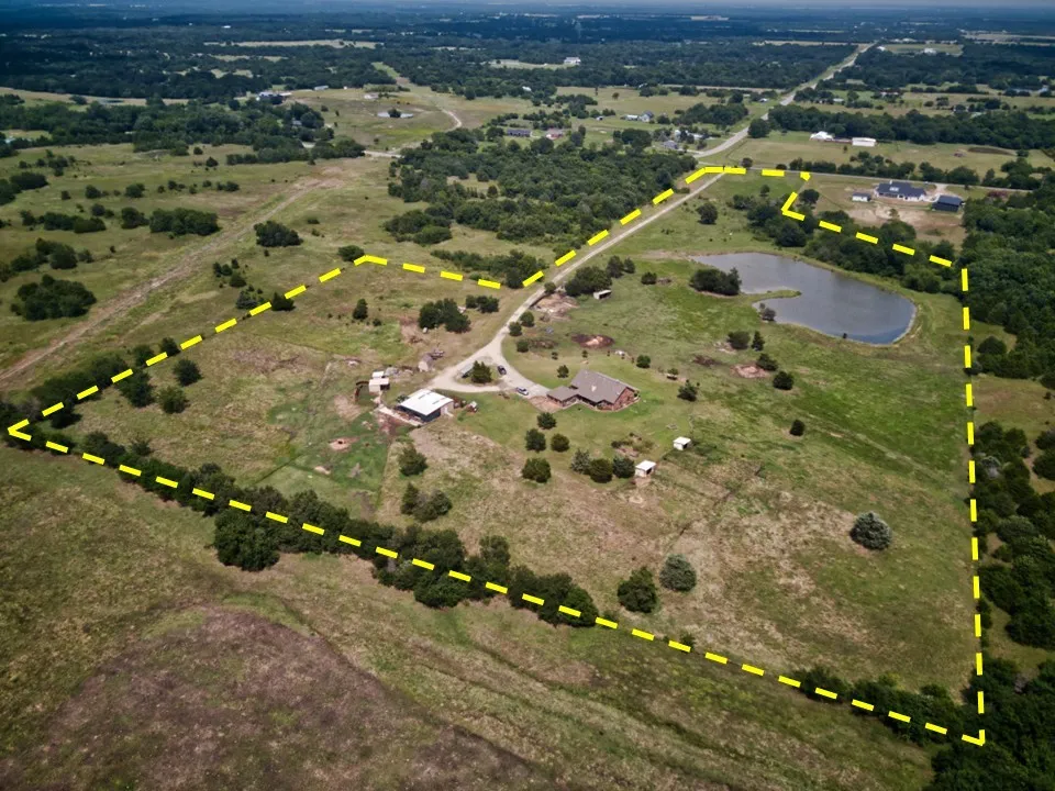 Expansive rural property featuring a large pond, extensive green acreage, perimeter tree lines, and a residential structure with an accompanying outbuilding