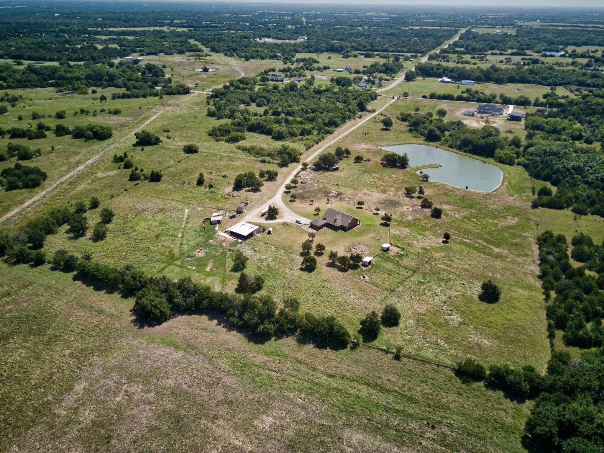 Expansive rural property featuring a main residence with a brown roof, an auxiliary structure, and a private pond