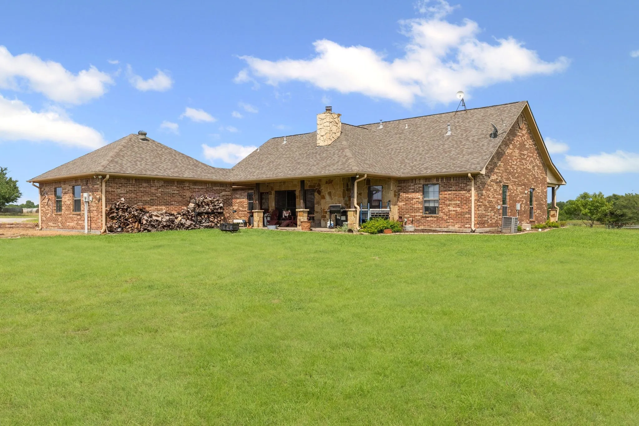 Expansive green lawn surrounds a brick residence with a covered patio