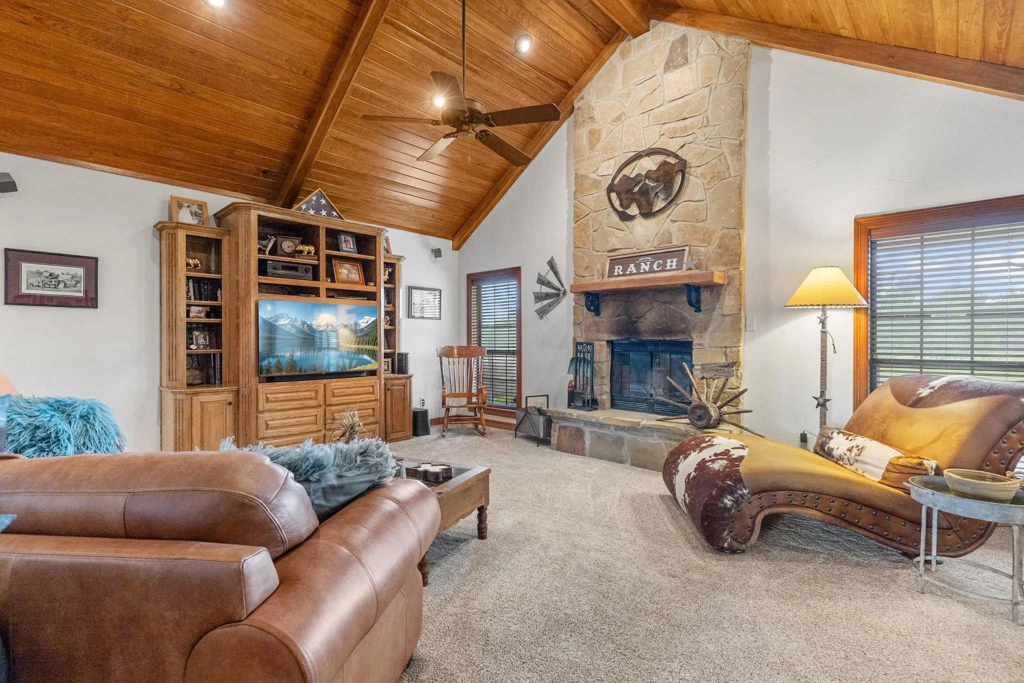 Vaulted wood-paneled ceiling with exposed beam accents, stone-clad fireplace with mantel, built-in entertainment center, and expansive windows