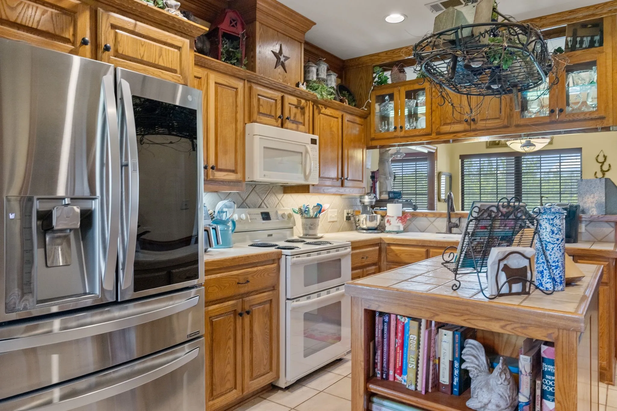 Kitchen featuring wood cabinetry, a stainless steel refrigerator, white tile flooring, a built-in double oven, and a tiled kitchen island with open shelving
