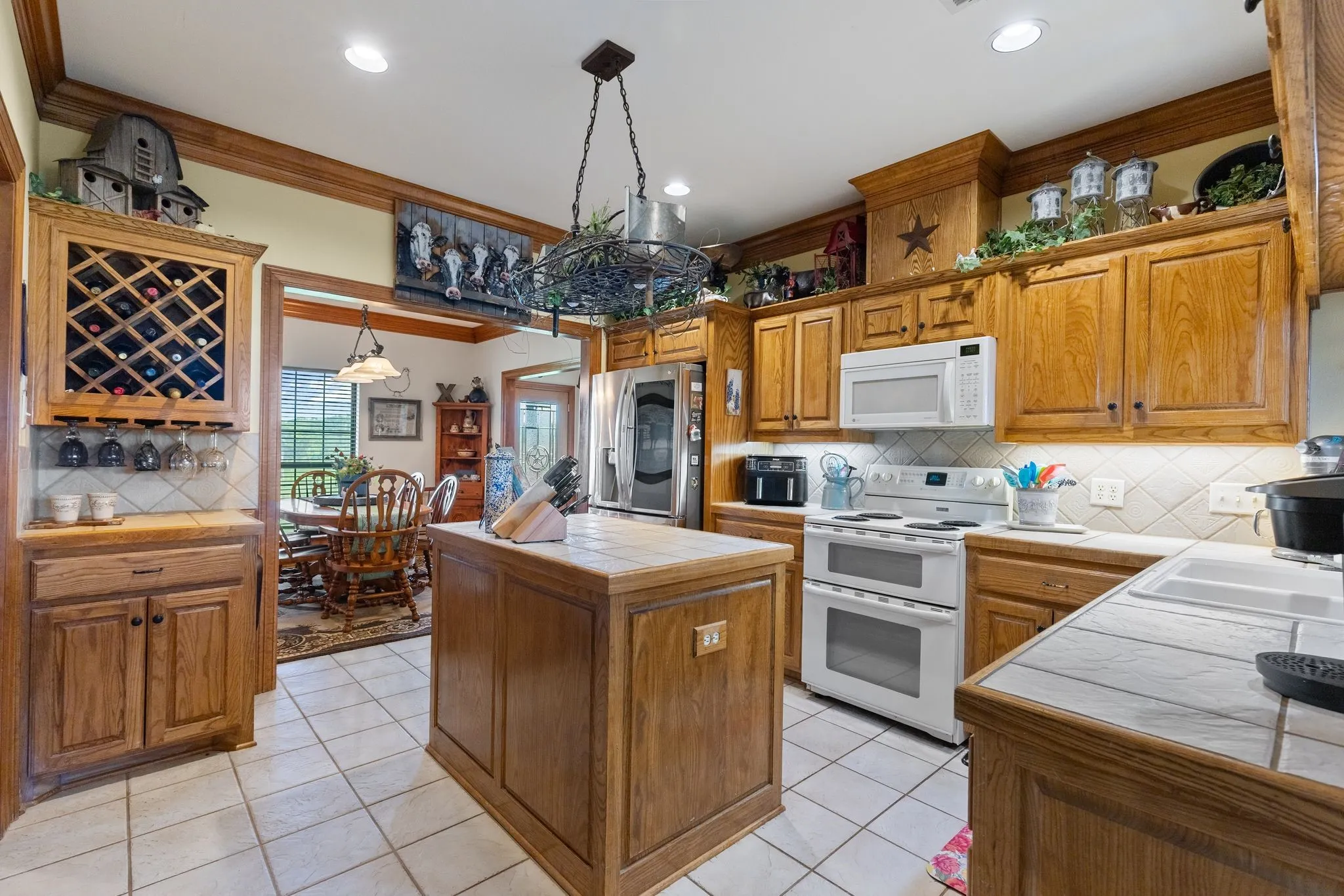 Kitchen featuring wood cabinetry, tile countertops, stainless steel refrigerator, white electric range with double ovens, and a built-in wine rack