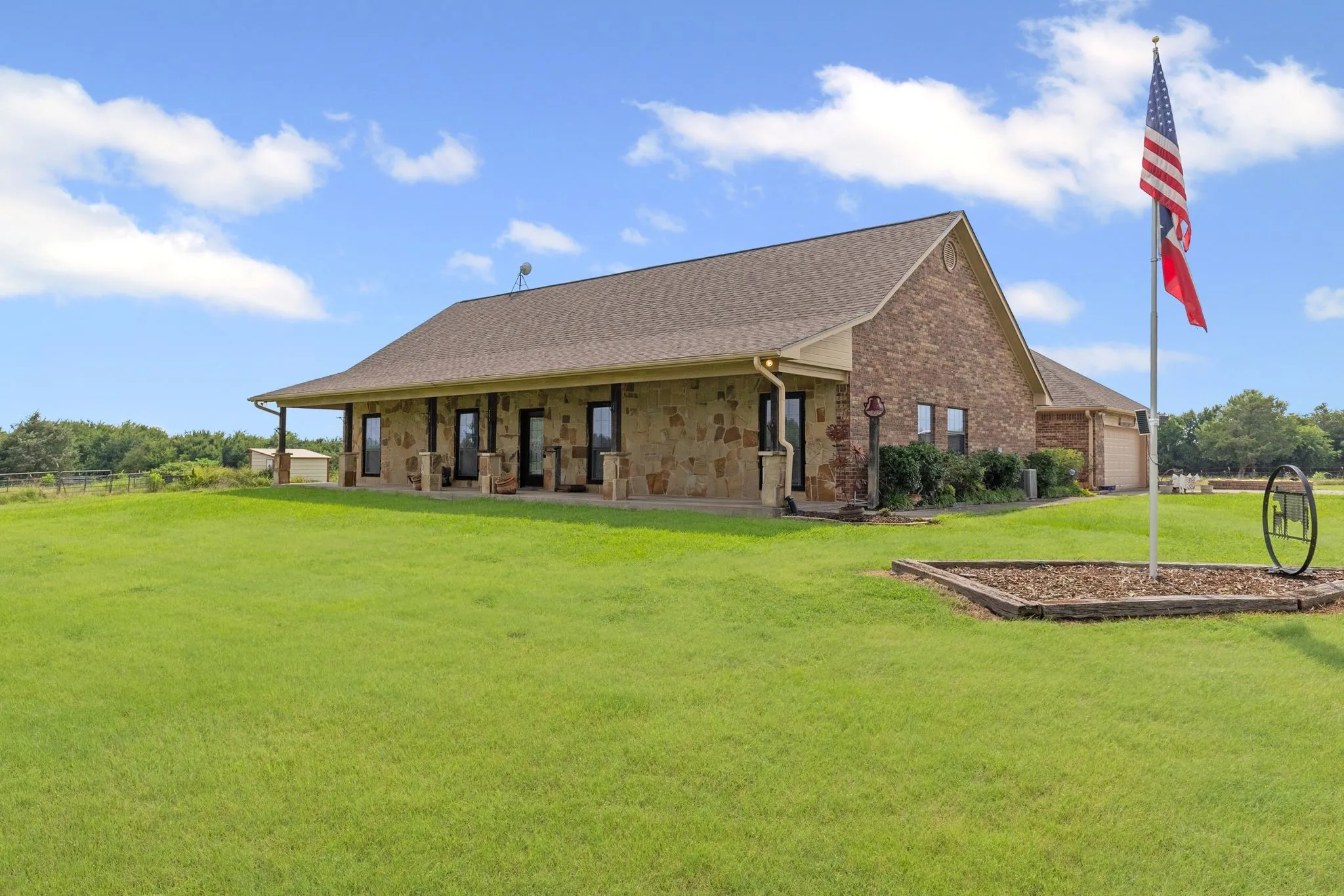 View of residence front porch and small flower bed around flag pole.