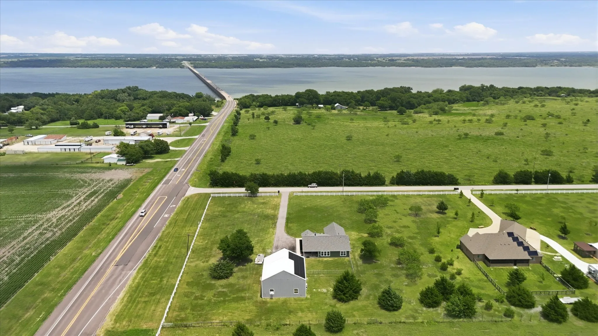 Expansive property with a large body of water in the background, featuring multiple buildings, a paved road, and a bridge