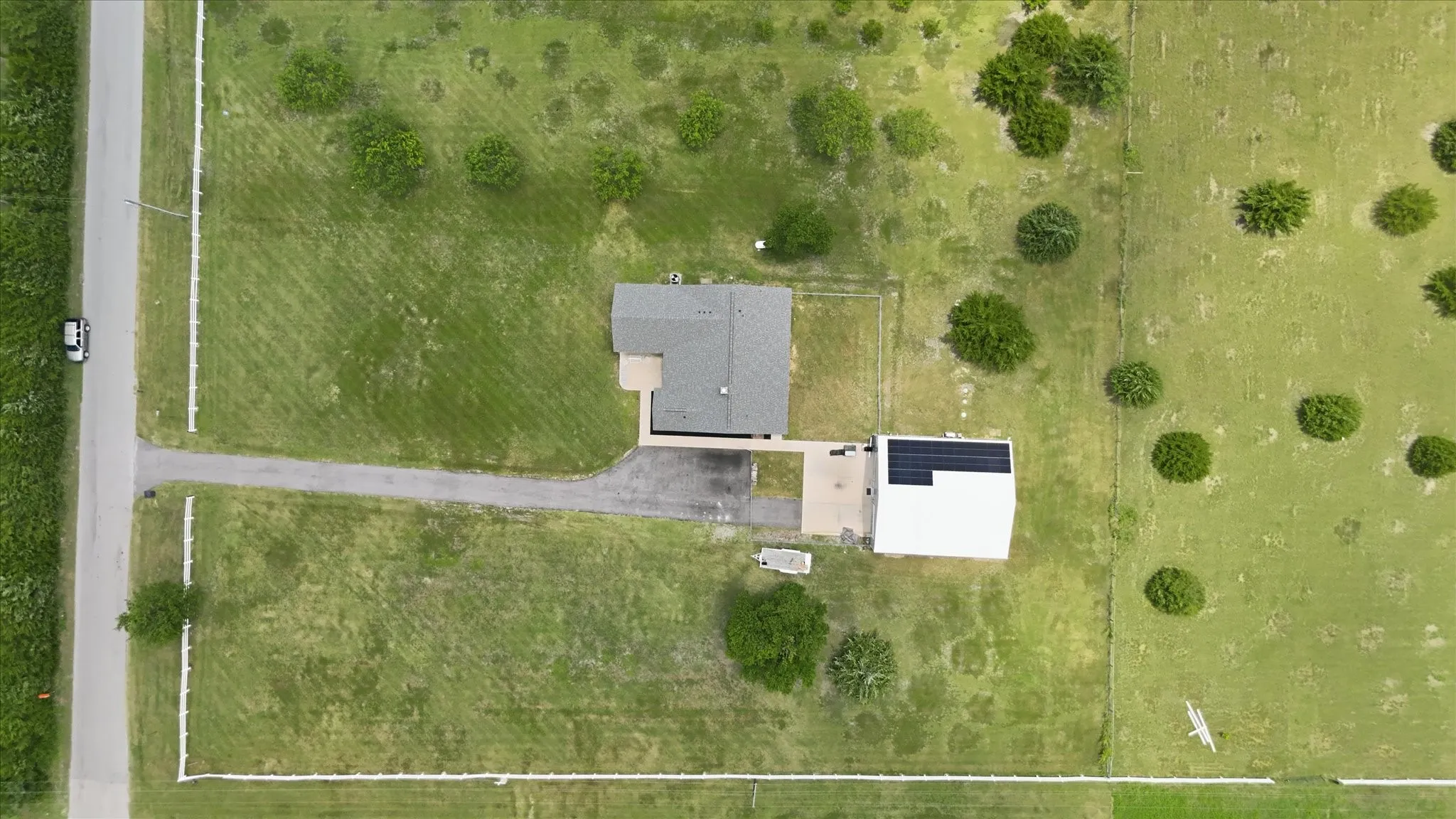 Expansive property featuring a main residence with a gray shingle roof, a secondary structure with a white roof, solar panels, and a paved driveway