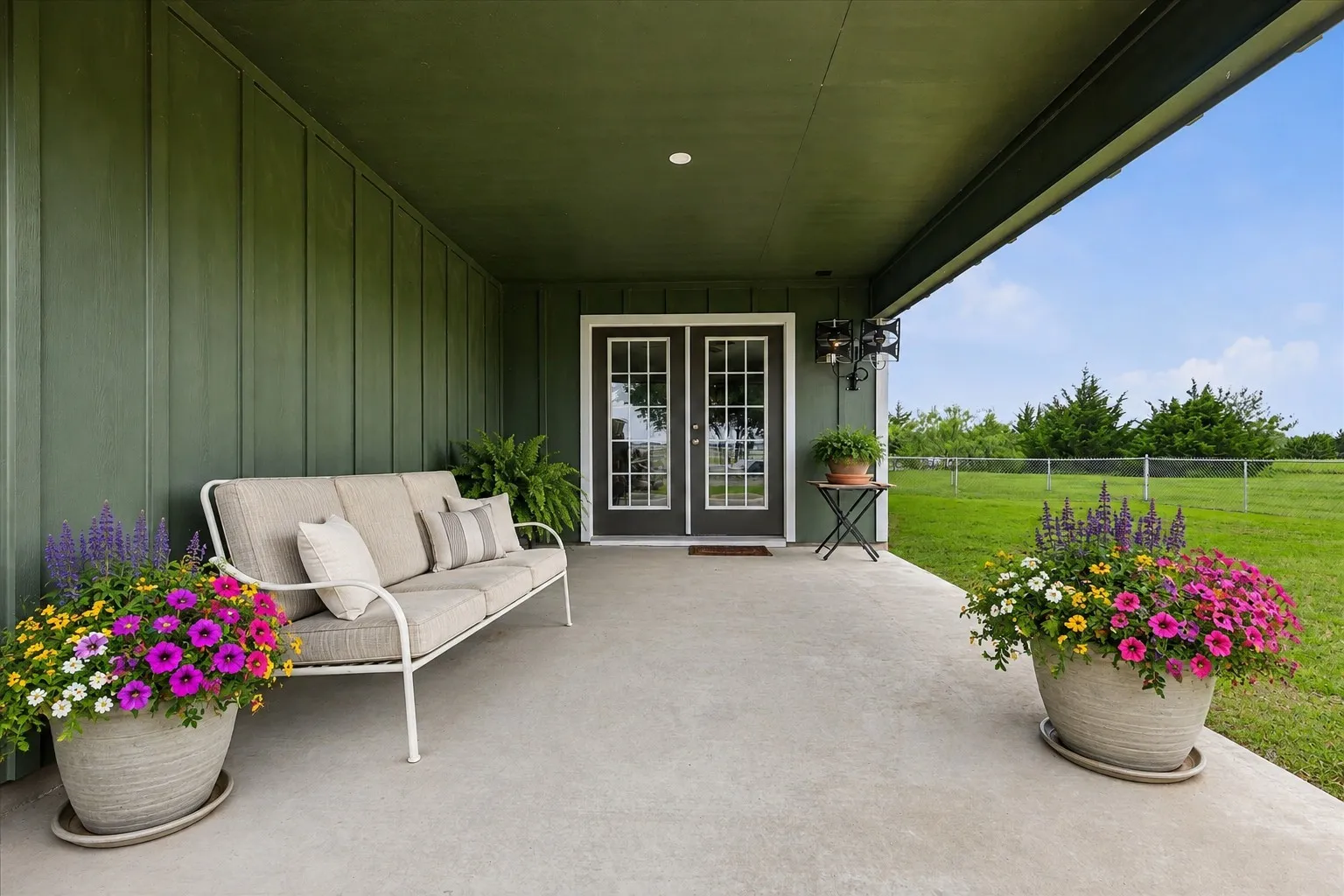 Virtually Staged Covered concrete patio featuring board and batten siding and exterior lighting