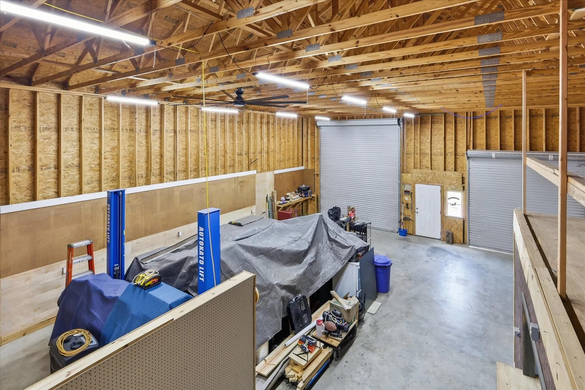Spacious unfinished interior featuring exposed wood trusses, concrete flooring, and multiple roll-up garage doors
