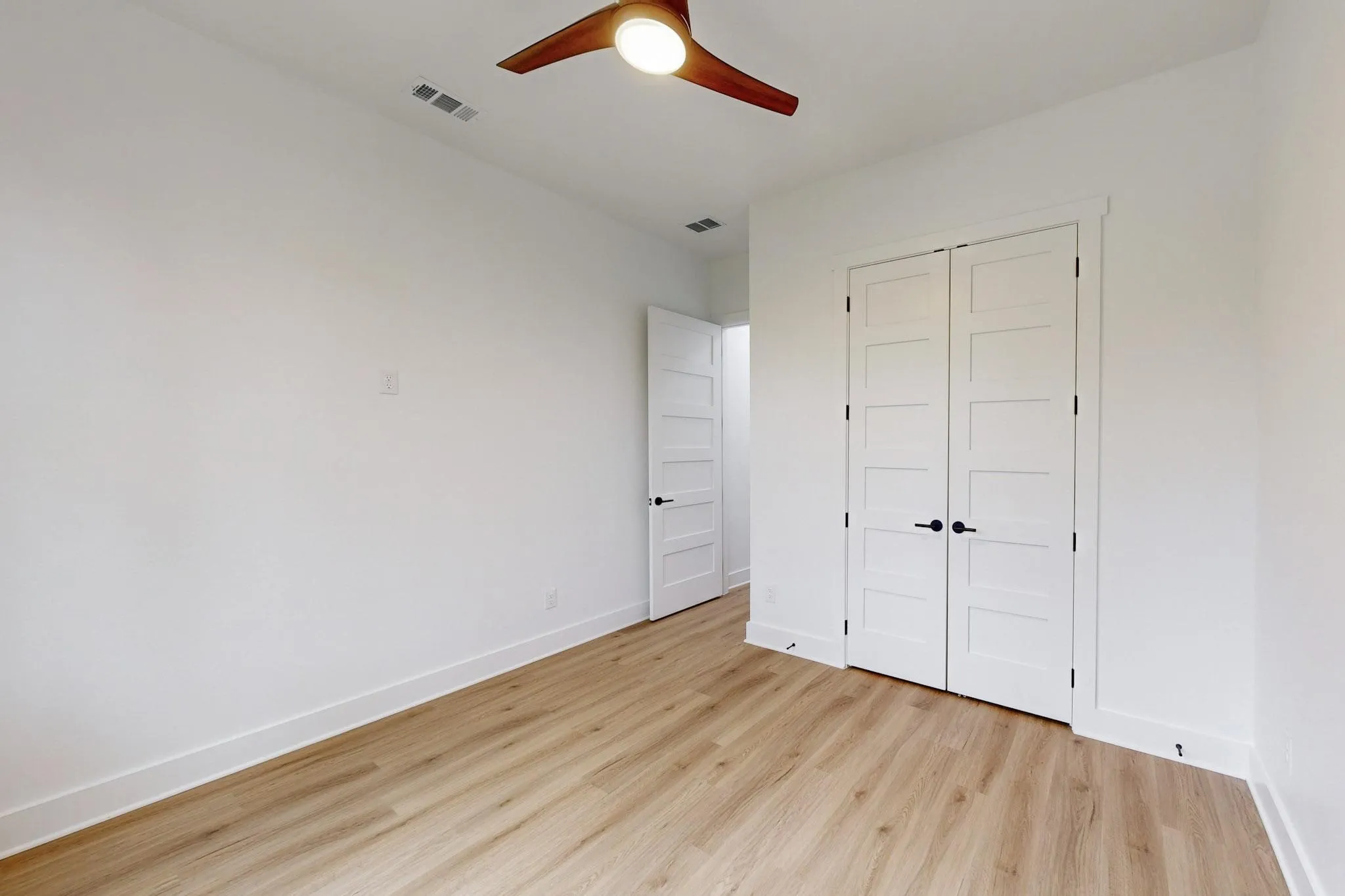 Interior room featuring light wood-finish flooring, white walls, and a ceiling fan with wood-tone blades