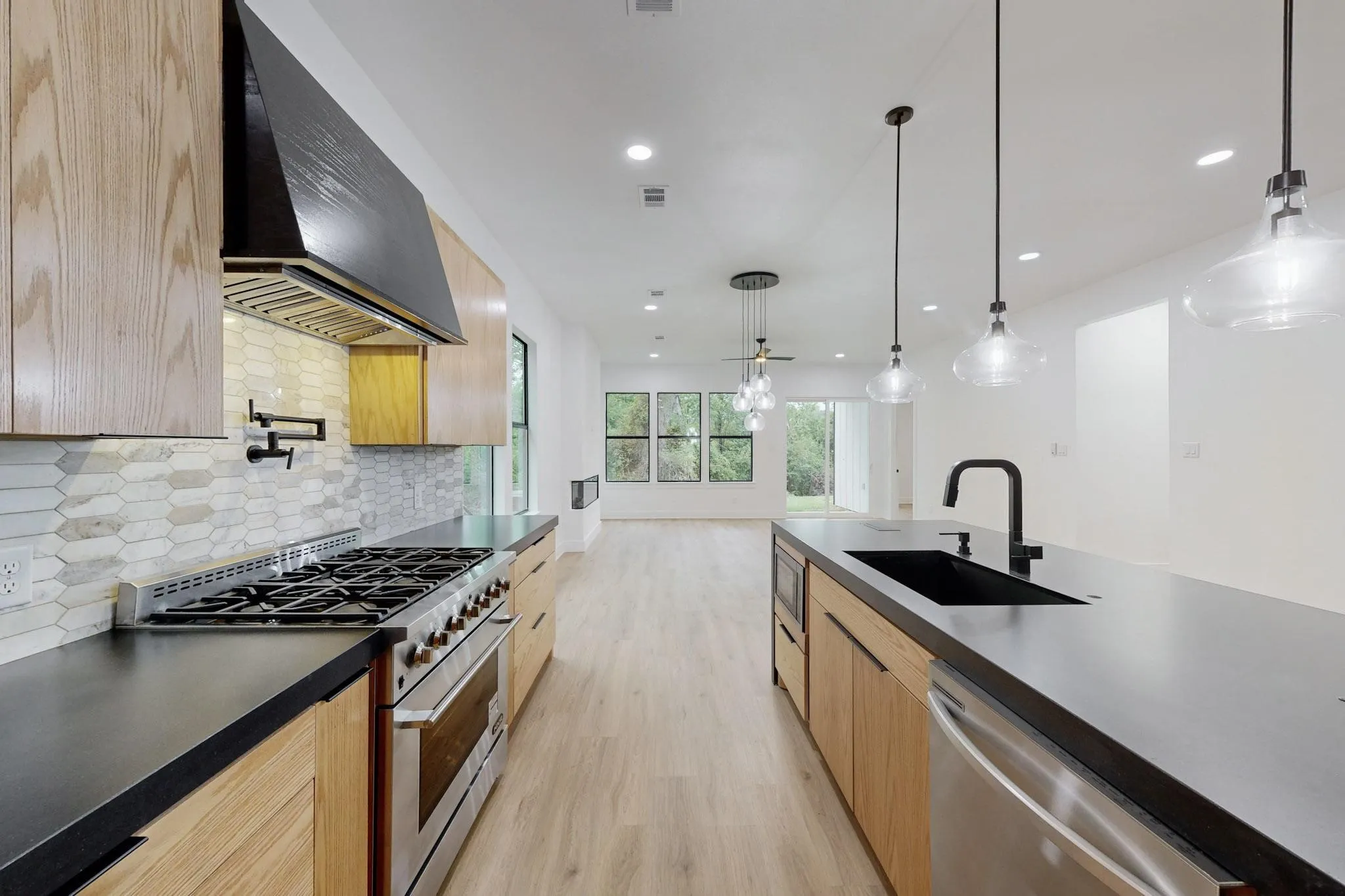 Modern kitchen featuring light wood-finish cabinetry, dark countertops, and a full stainless steel range with a pot filler faucet