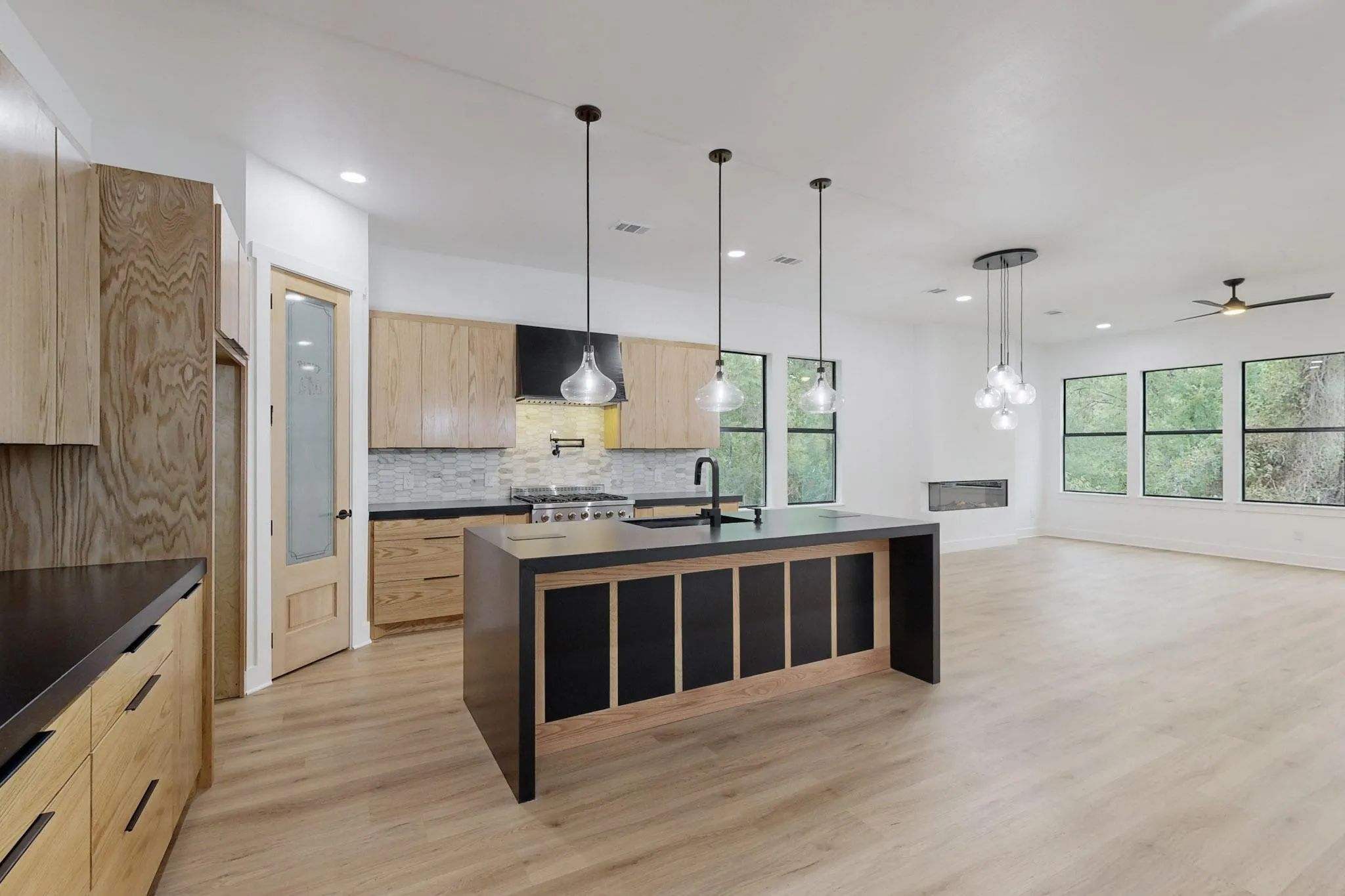 Expansive kitchen and living area featuring a central island with pendant lighting, light wood-finish flooring, a modern fireplace, and multiple large windows