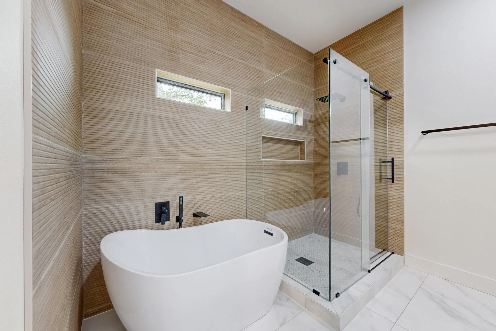 Freestanding soaking tub with matte black fixtures, glass-enclosed shower, and textured tile wall